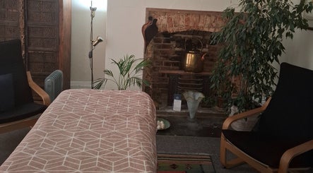 Relaxation room at Shass Therapy Massage, Cheltenham, England featuring a massage table, armchair, and brick fireplace.