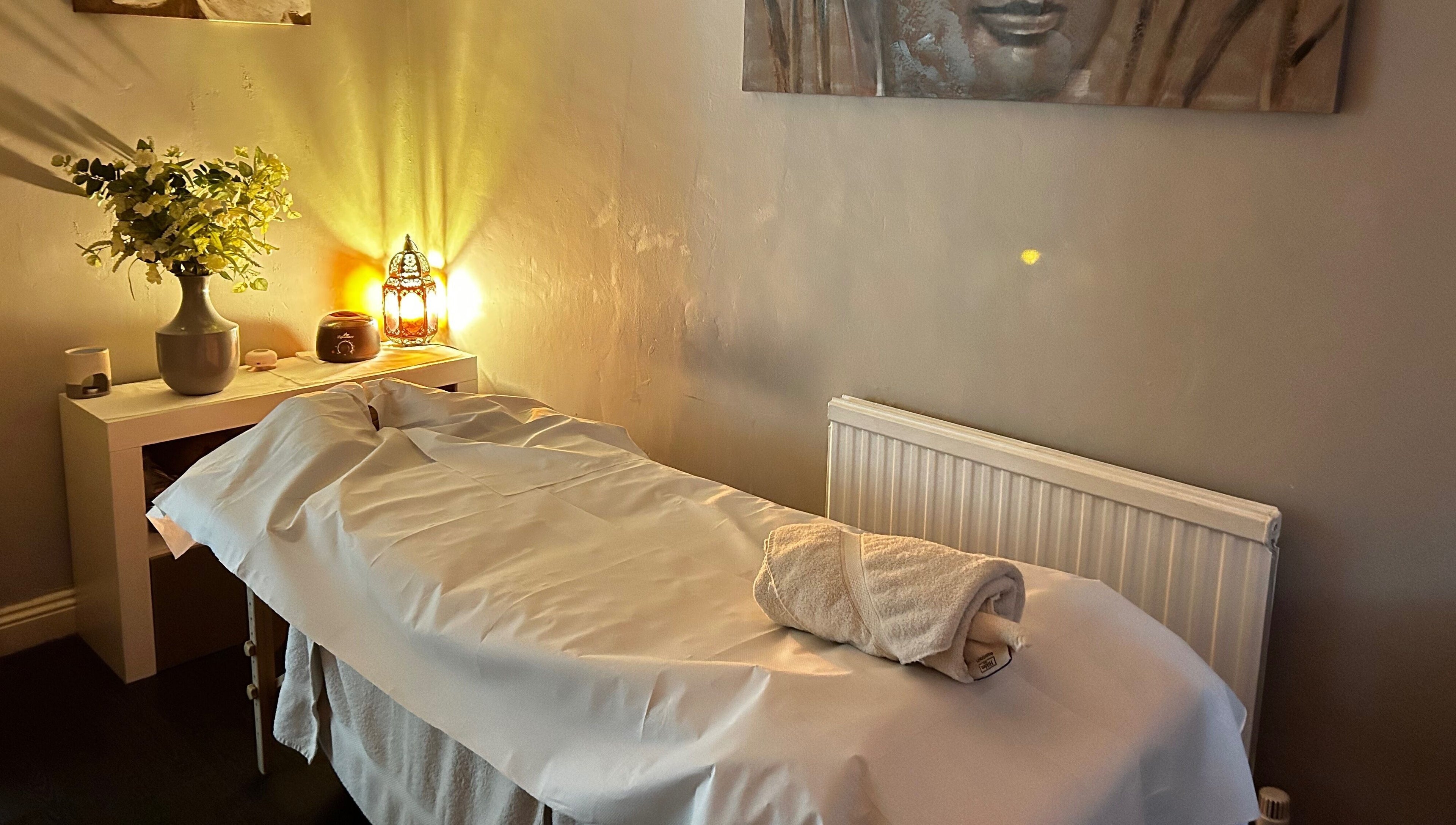 Peaceful massage room at Hands of Buddha, Sale, England, GB with warm lighting and fresh flowers.