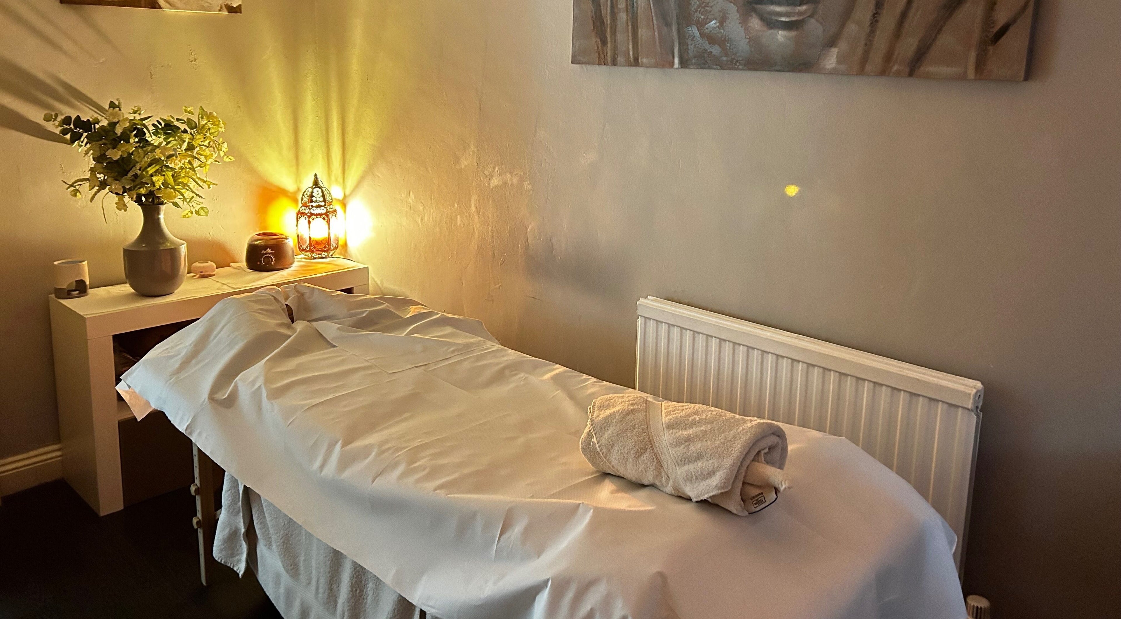 Peaceful massage room at Hands of Buddha, Sale, England, GB with warm lighting and fresh flowers.
