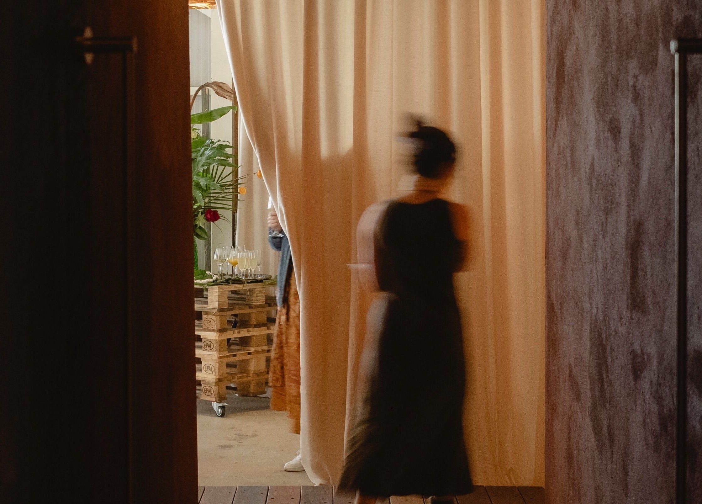 A woman walking through curtain into Kondōu in Kincumber, New South Wales, AU, with plants and wine glasses visible.