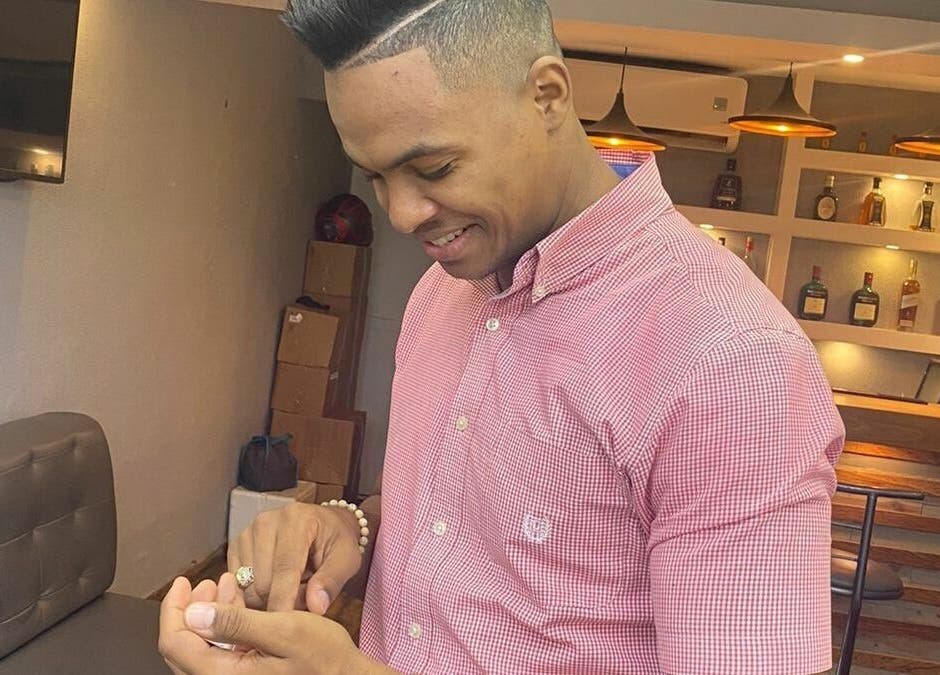 A smiling man at Guelo Barber Studio in Santo Domingo, DO, holding a small item, with a modern interior backdrop.