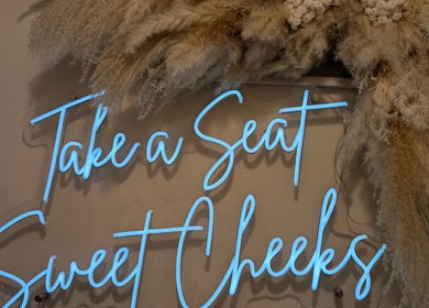 Blue neon sign saying 'Take a Seat Sweet Cheeks' at Hair by Karina Brown, Leeds, England, GB.
