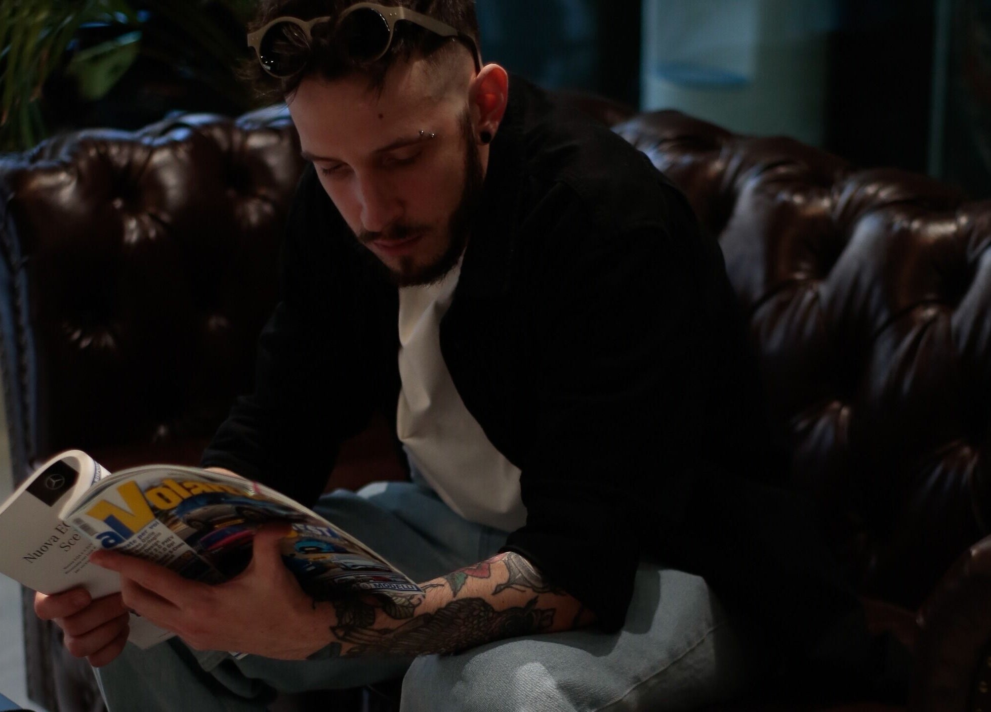 Cliente rilassato al Barber Lounge, Milano, Lombardia, IT, su divano di pelle mentre legge una rivista.