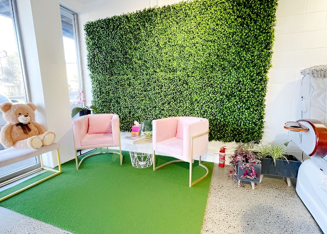 Chic waiting area with pink chairs at Nail Magic, Auckland, NZ, featuring a lush green wall.