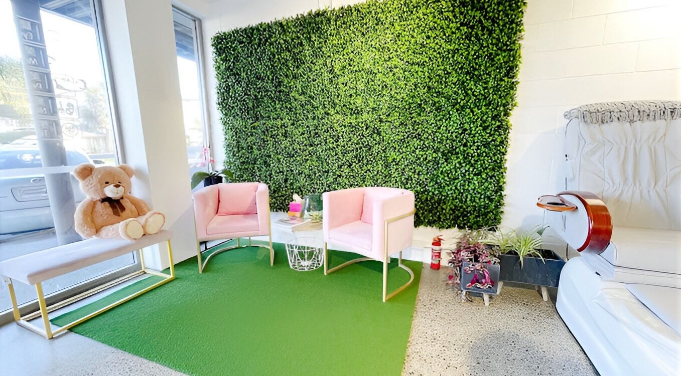 Chic waiting area with pink chairs at Nail Magic, Auckland, NZ, featuring a lush green wall.