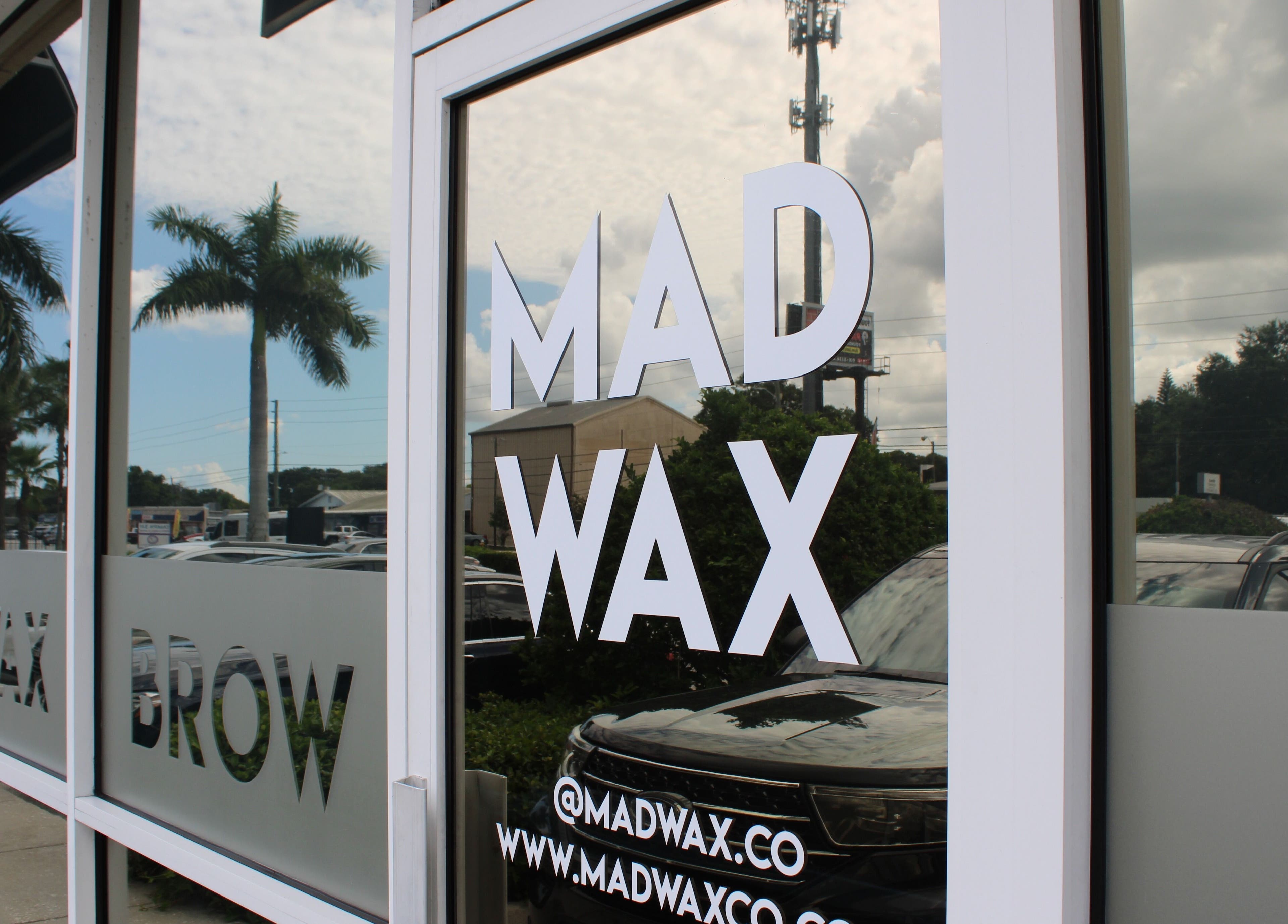 Exterior glass door of Mad Wax in Largo, Florida, US, reflecting palm trees and sky.