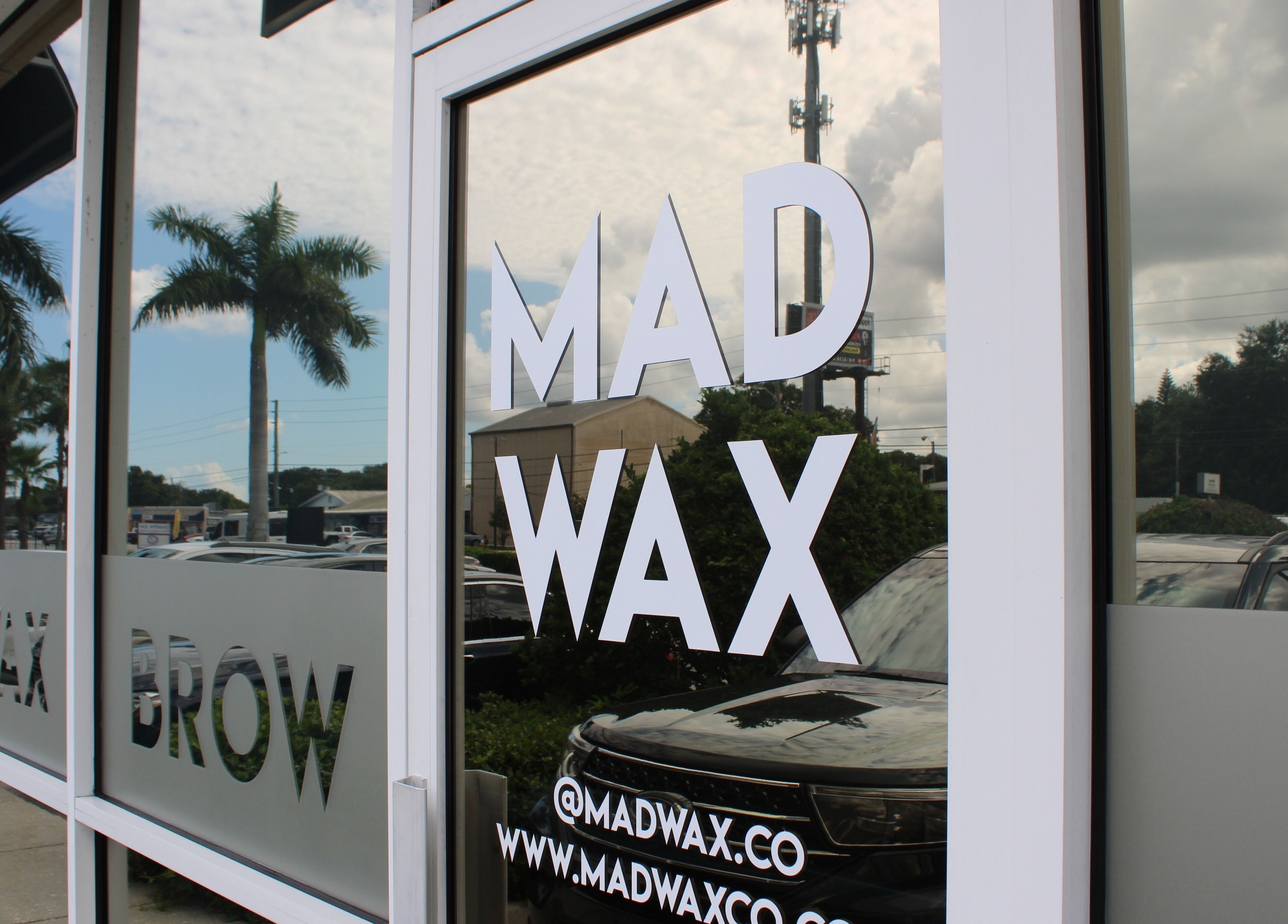 Exterior glass door of Mad Wax in Largo, Florida, US, reflecting palm trees and sky.