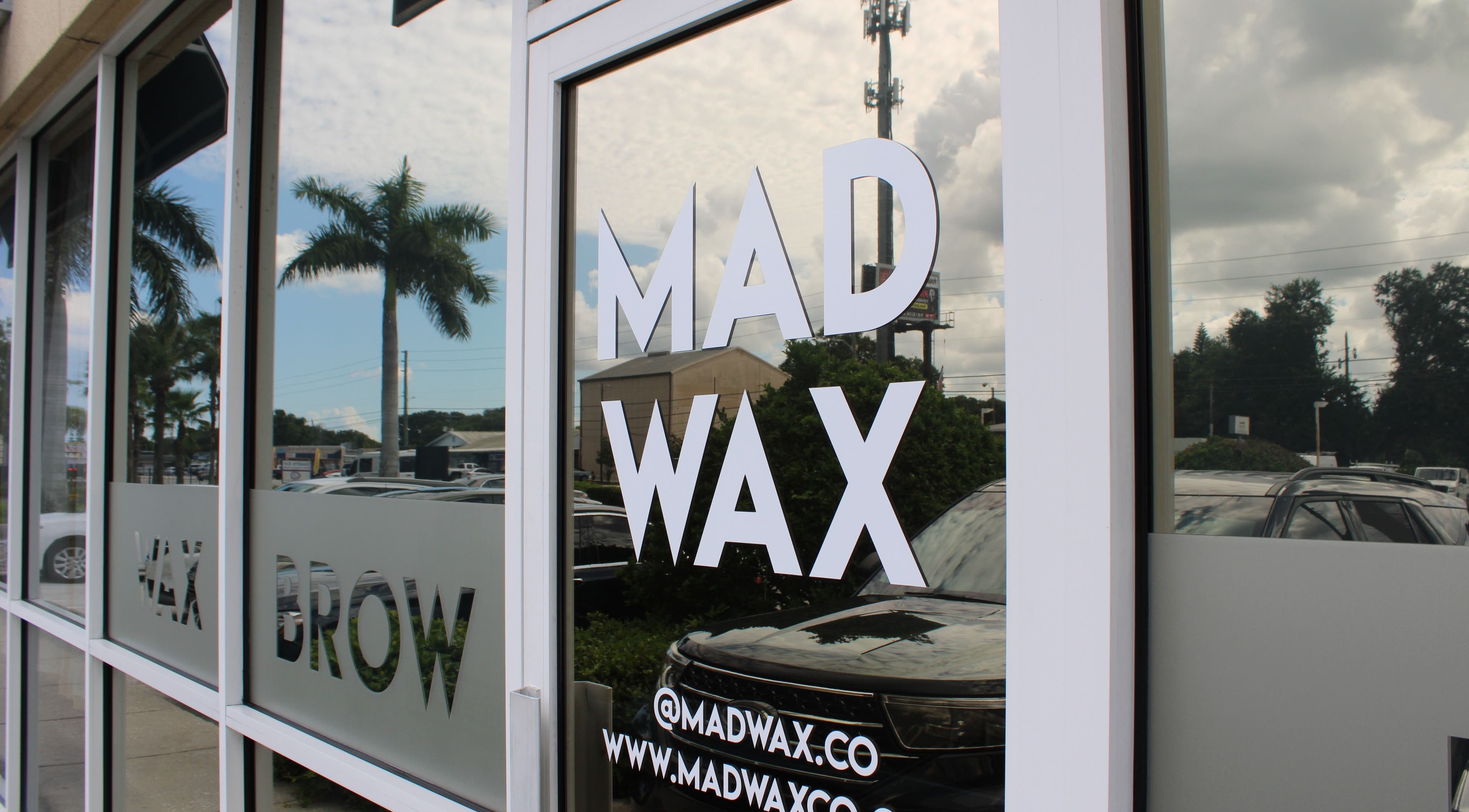 Exterior glass door of Mad Wax in Largo, Florida, US, reflecting palm trees and sky.