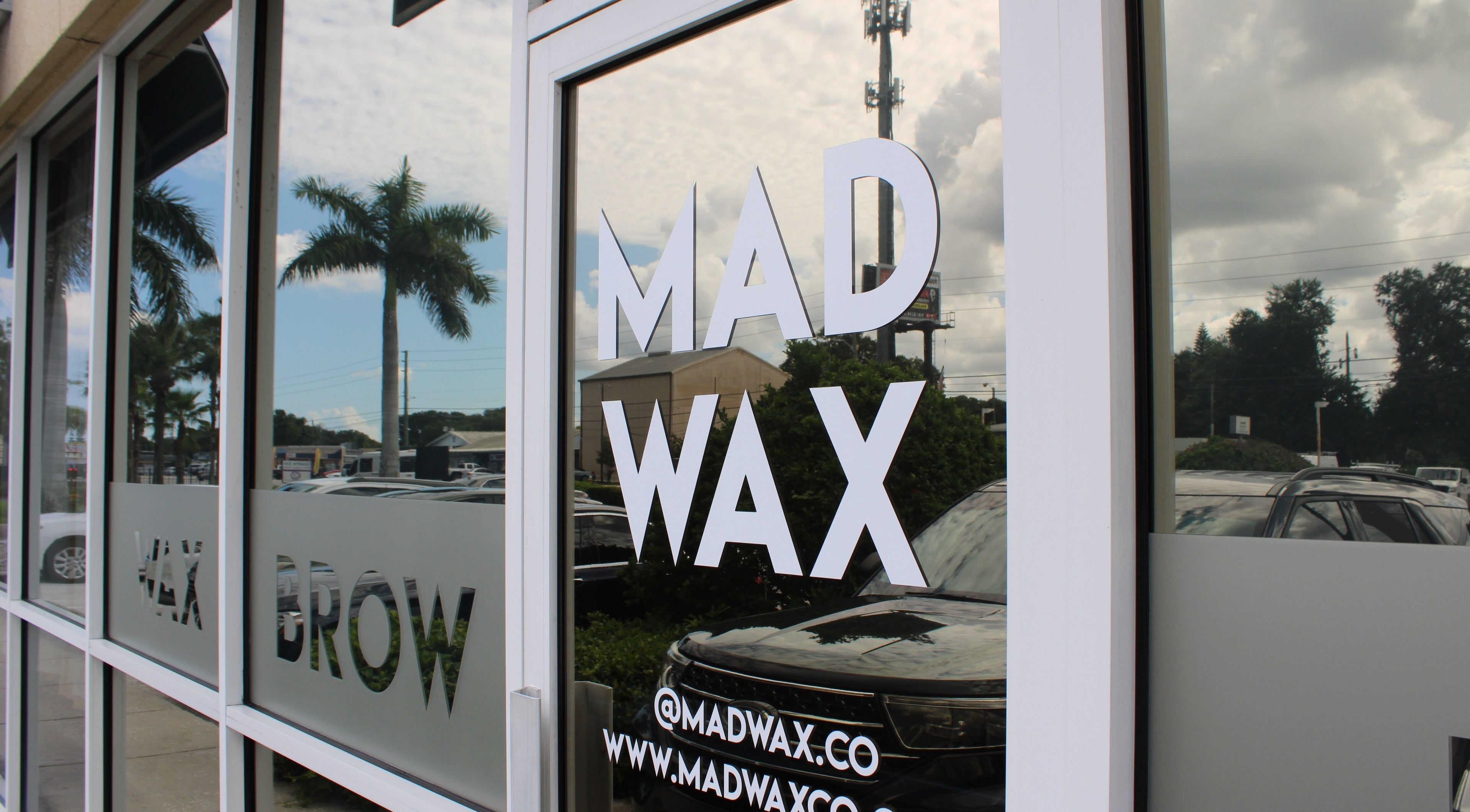 Exterior glass door of Mad Wax in Largo, Florida, US, reflecting palm trees and sky.