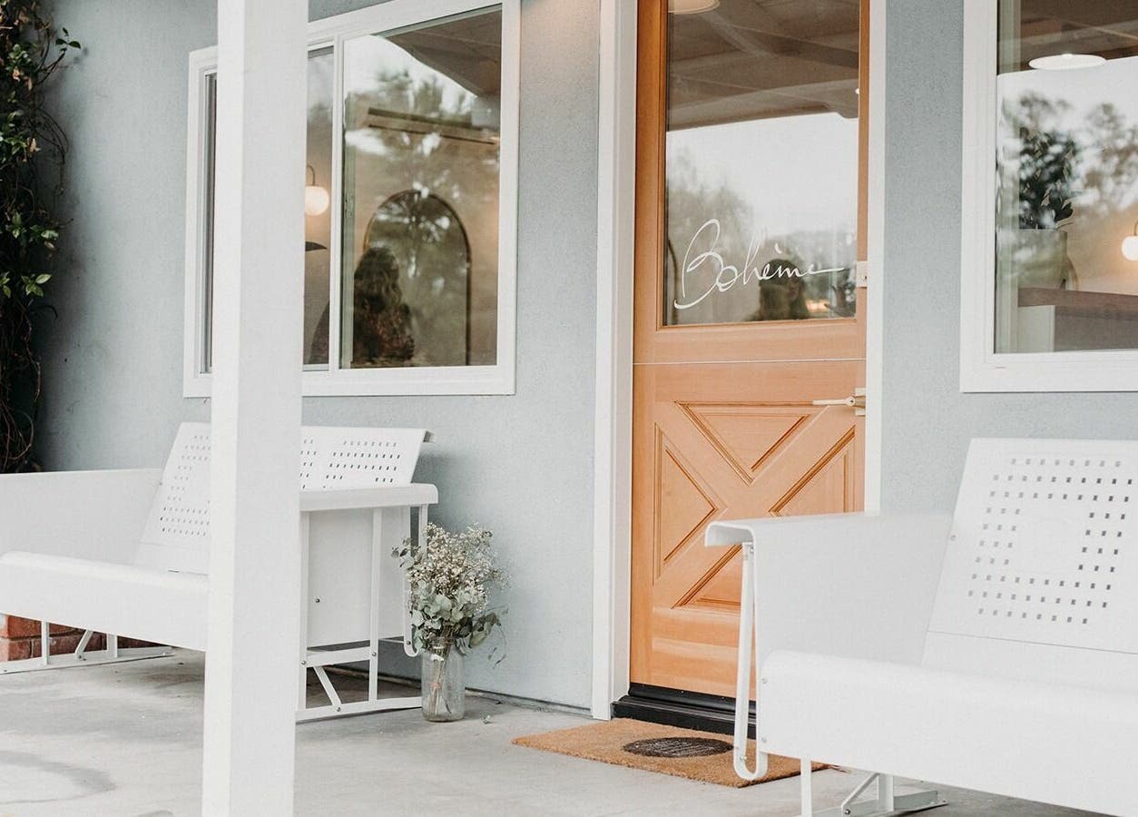 Charming entrance of Boheme in Ojai, California, US with white benches and a wooden door.