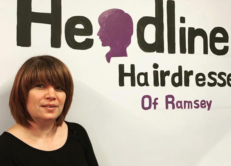 Stylist at Headlines salon in front of branded wall in Ramsey, England, GB.