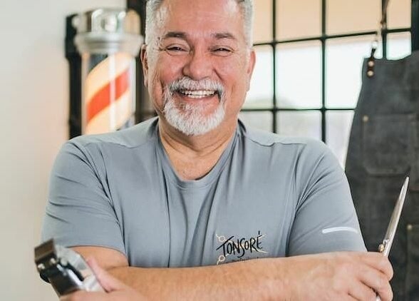 Barber at Tonsore Master Academy, San Antonio, Texas, US, holding shears and smiling warmly.