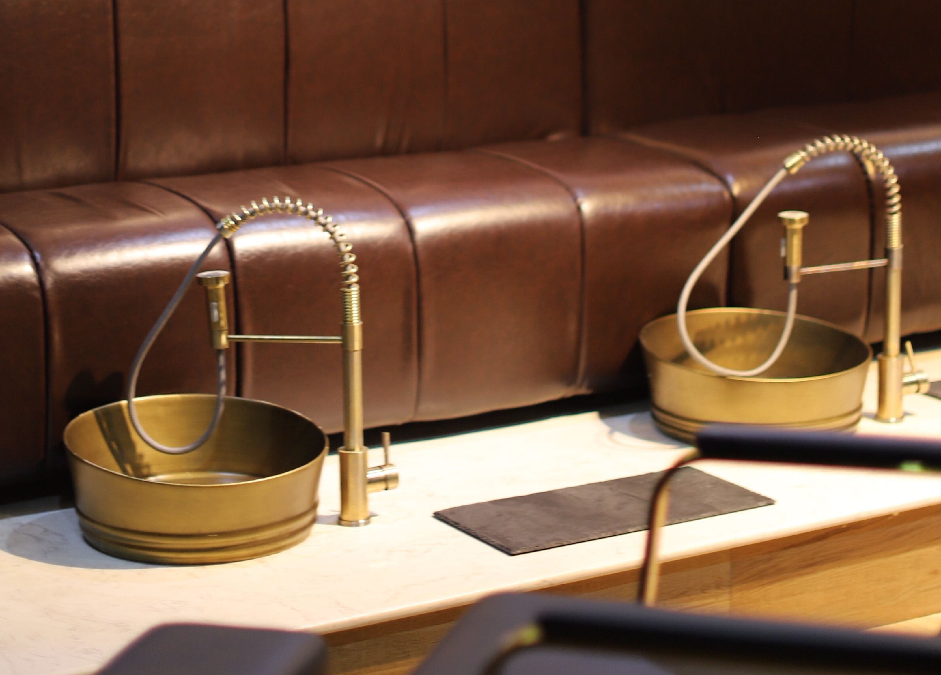 Luxurious pedicure area at VstylesHair & Beauty Studio, Ikeja, Lagos, NG with gold basins and brown seating.