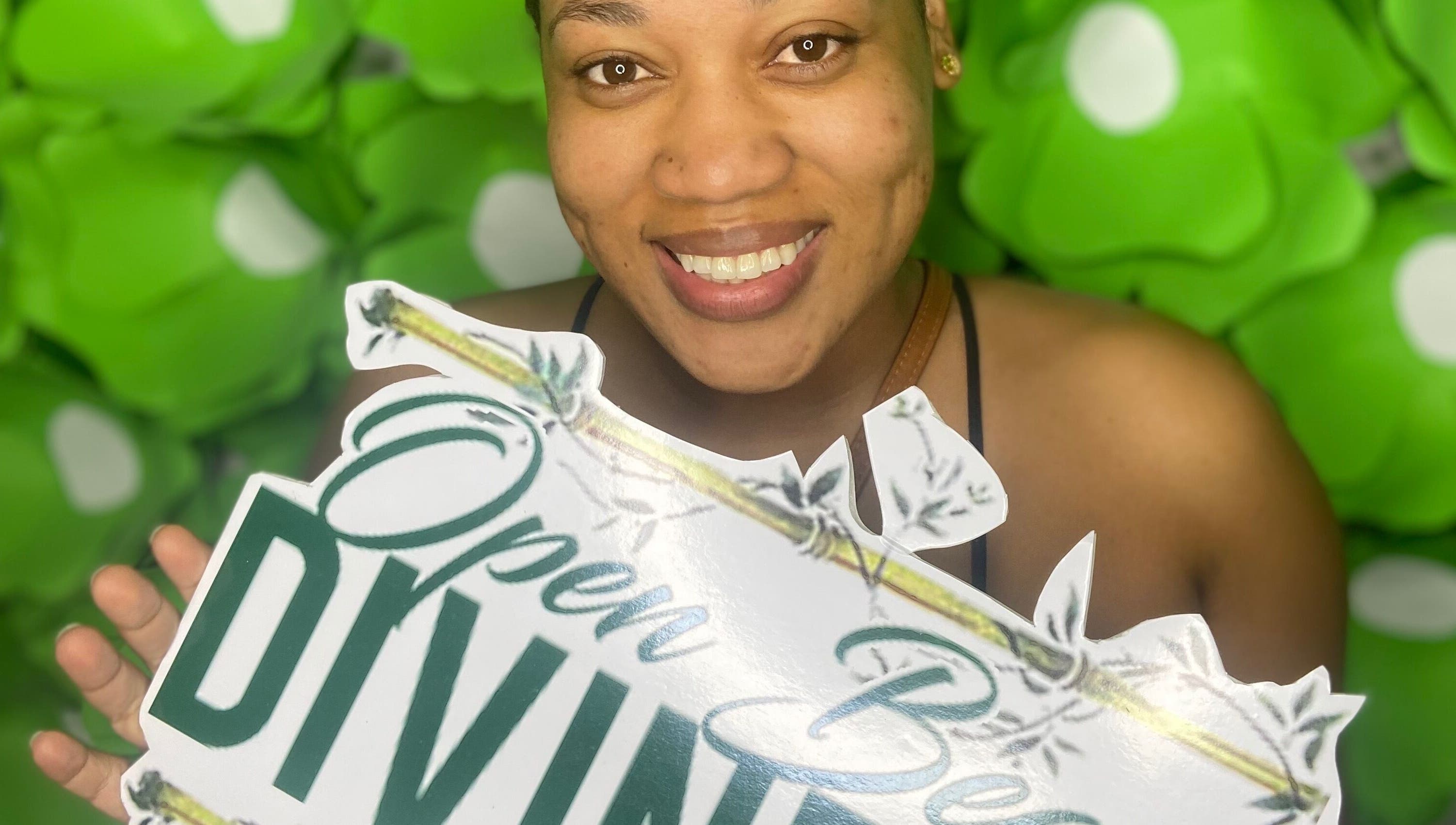 Smiling woman holds Open Beauty Divine Spa sign, Kingston, St. Andrew Parish, JM.