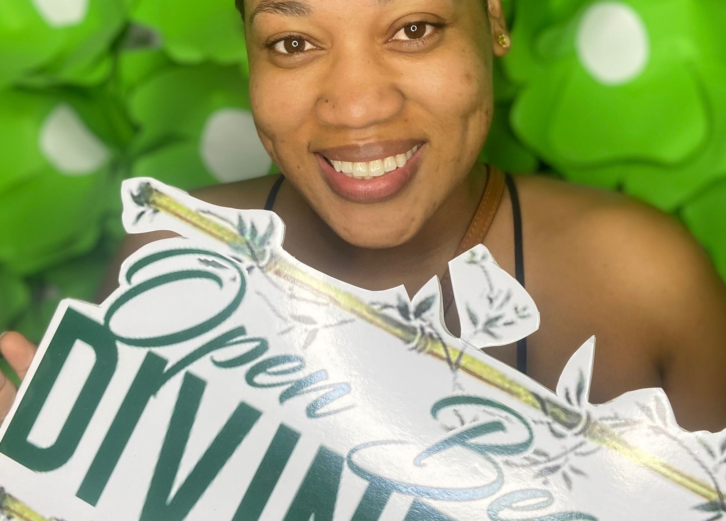 Smiling woman holds Open Beauty Divine Spa sign, Kingston, St. Andrew Parish, JM.