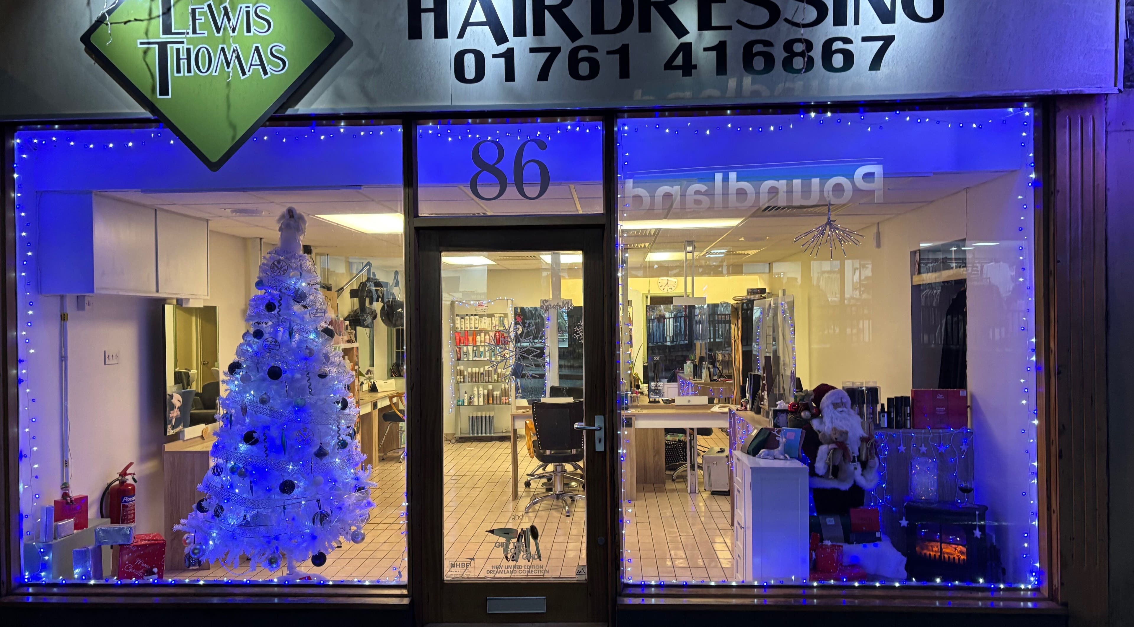Holiday-decorated front of Lewis Thomas Hairdressing, Midsomer Norton, England, GB with a white Christmas tree.