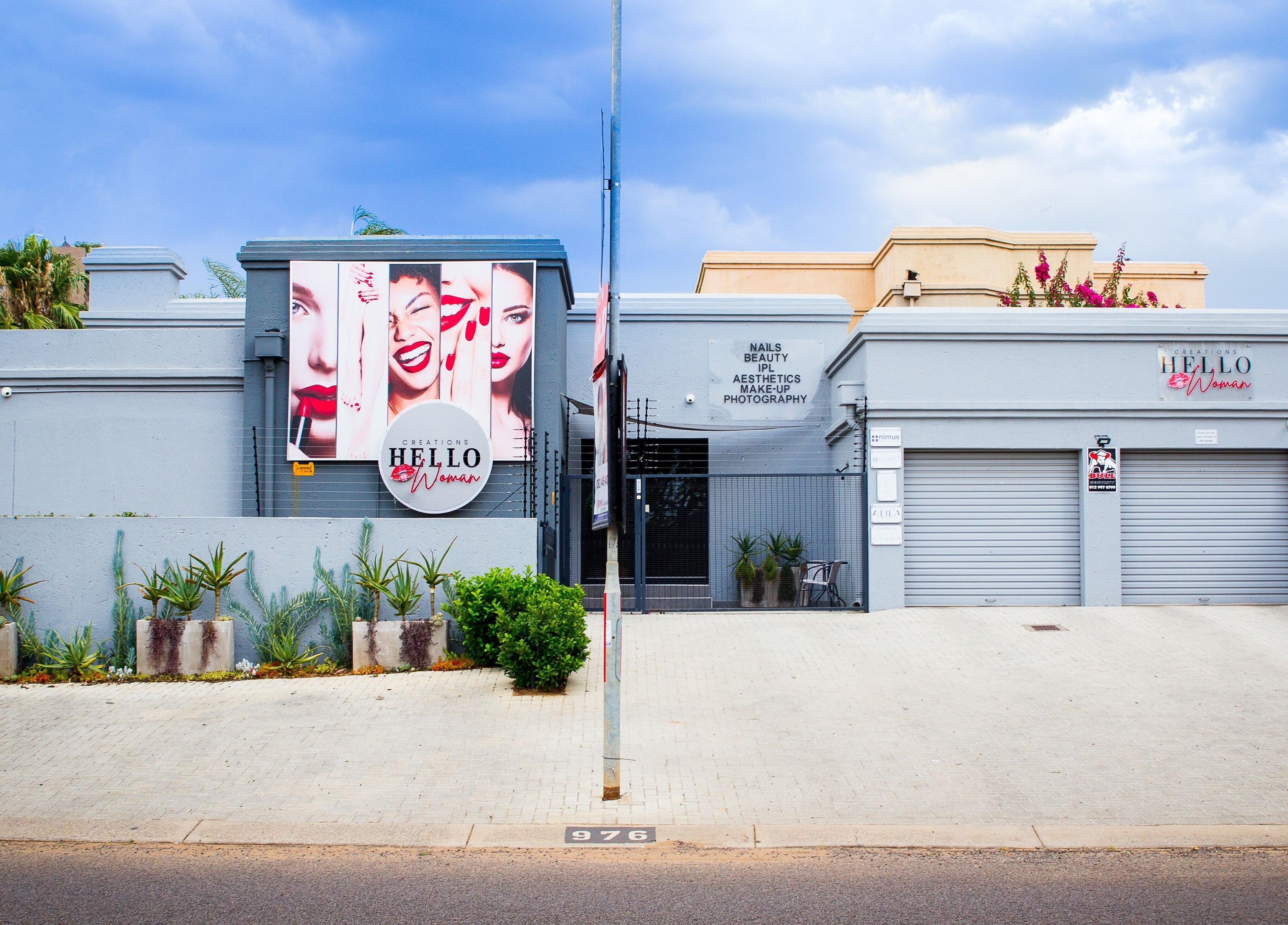Front view of HelloWoman Faerie Glen, a beauty venue in Pretoria, Gauteng, ZA with vibrant signs and plants.