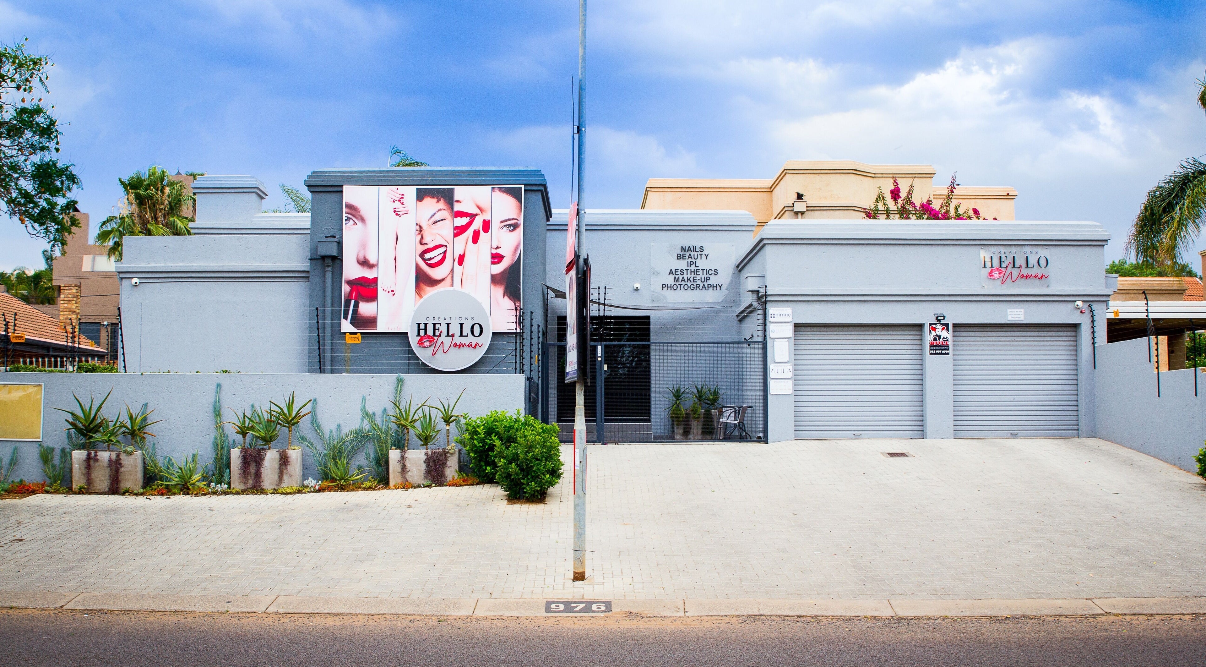 Front view of HelloWoman Faerie Glen, a beauty venue in Pretoria, Gauteng, ZA with vibrant signs and plants.