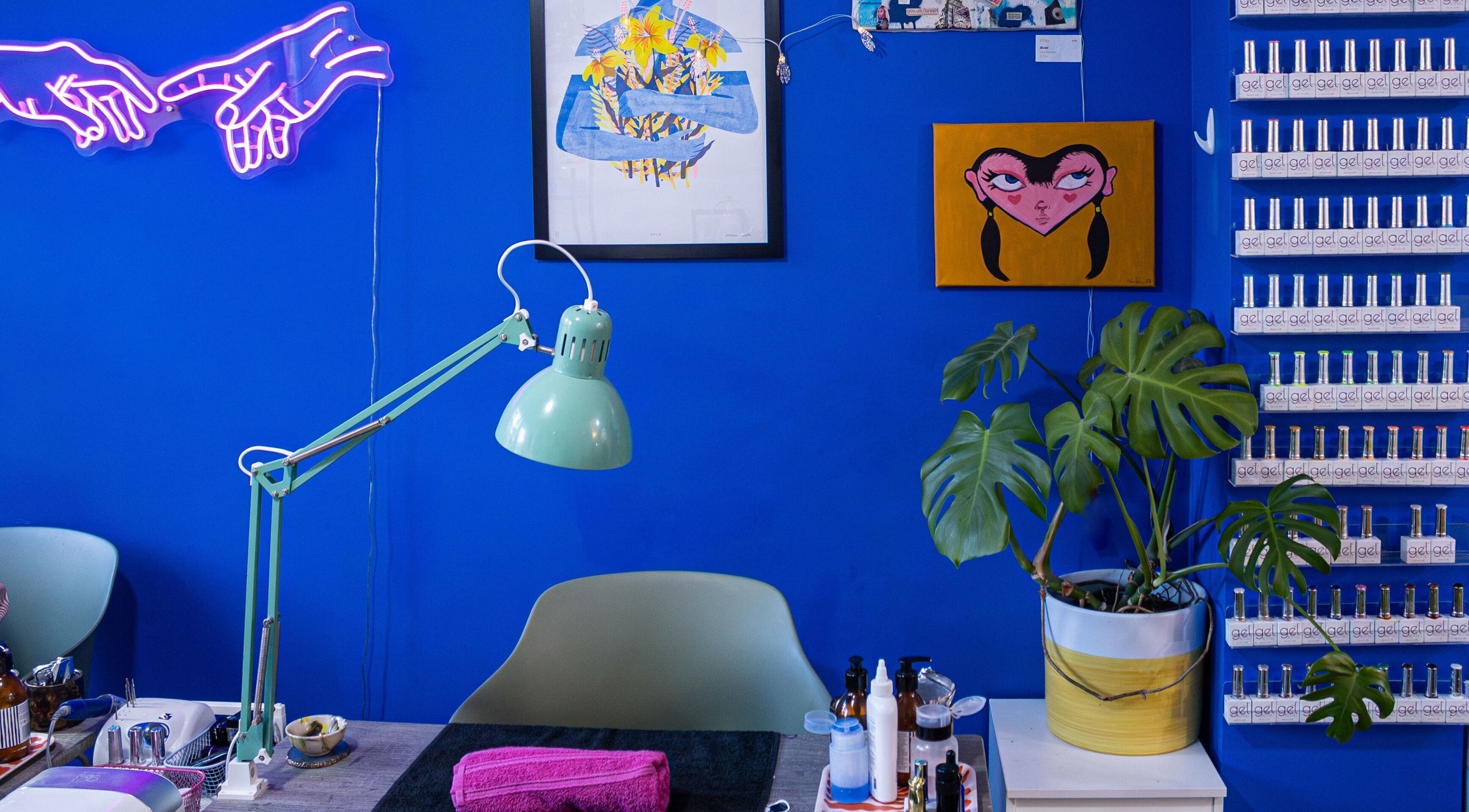 Tru Nail Art's vibrant workspace with blue walls in Brighton, England, GB. Features art, plants, and nail polishes.