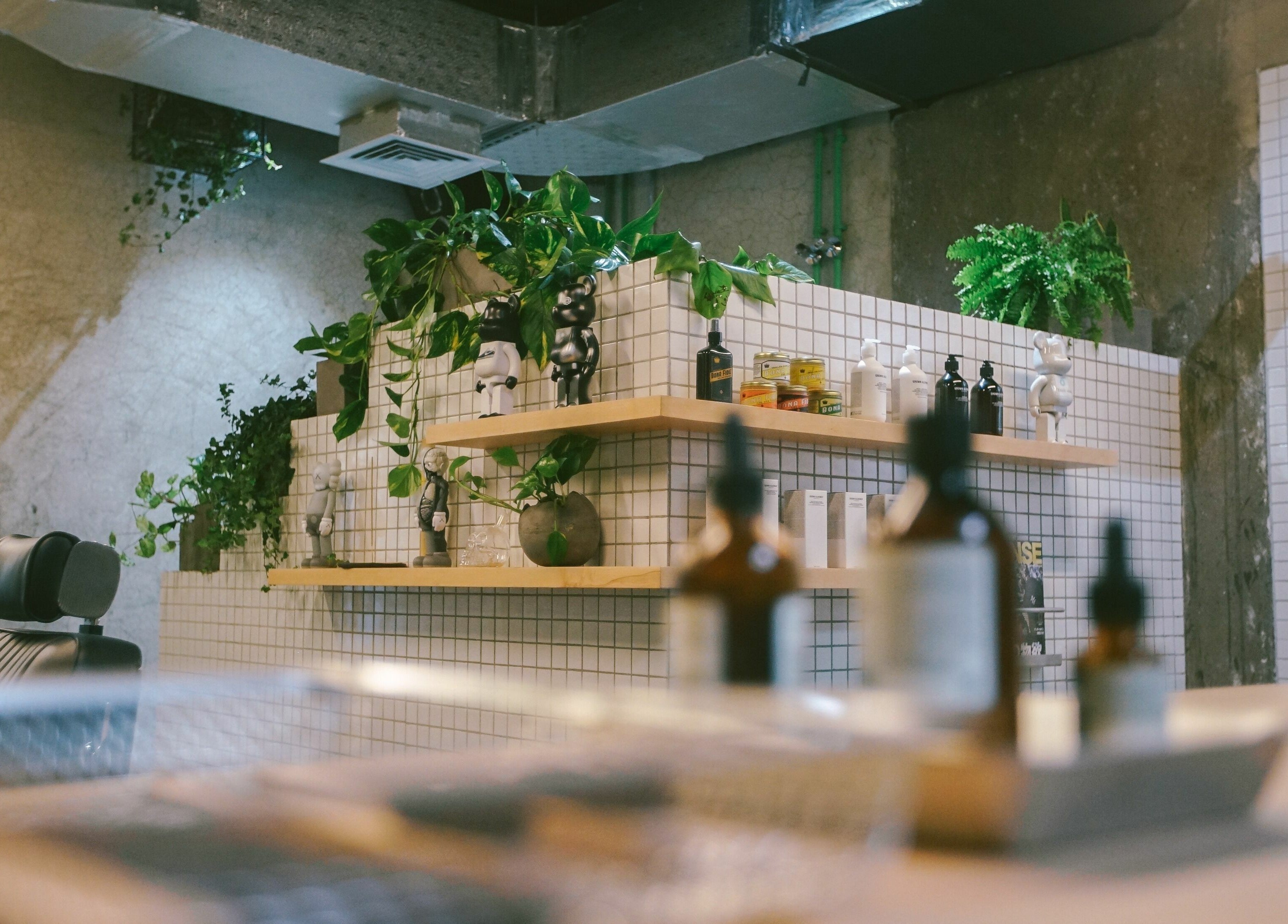 Amongst Few Barber in دبي, دبي, AE shows a stylish interior with green plants and grooming products on tiled shelves.