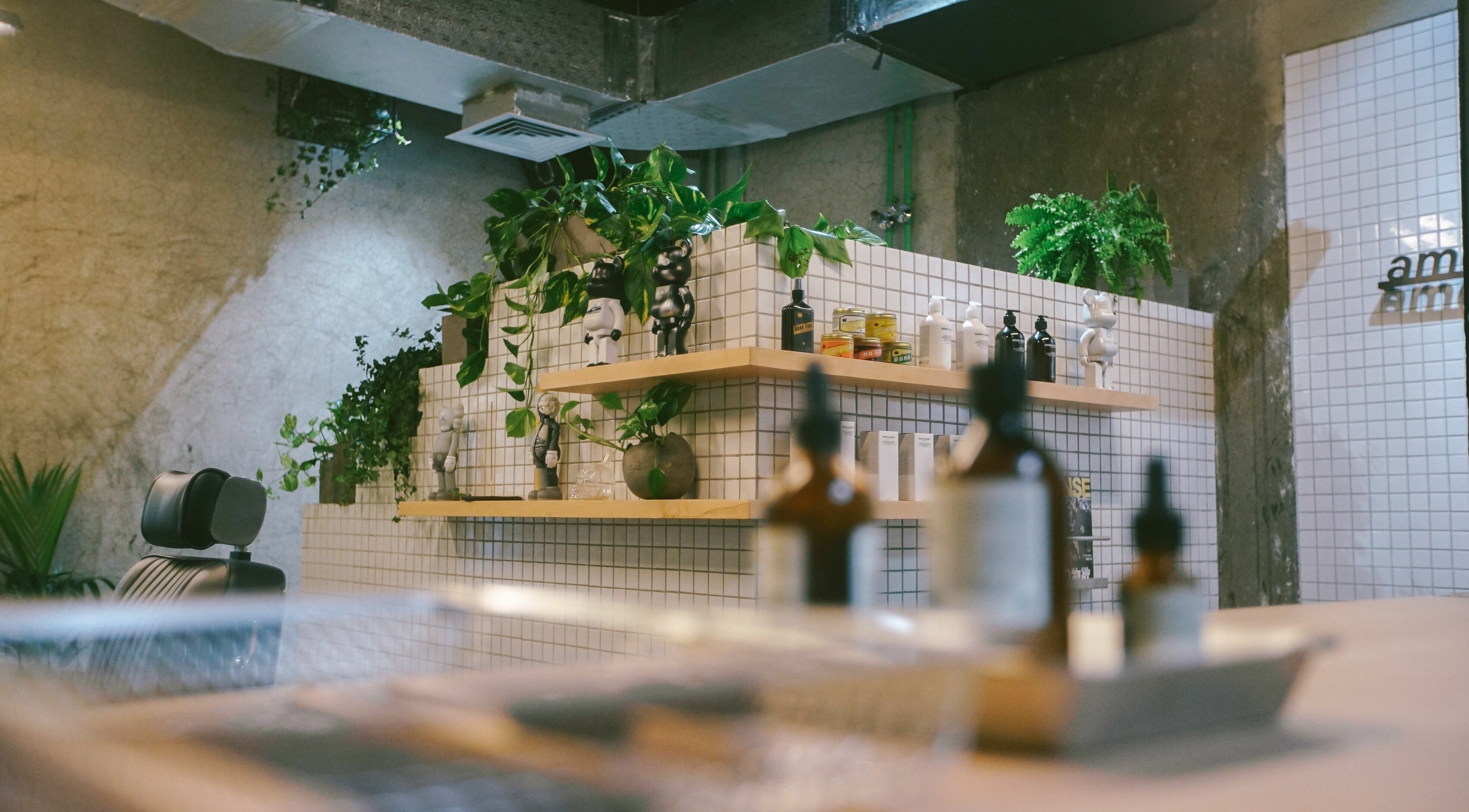 Amongst Few Barber in دبي, دبي, AE shows a stylish interior with green plants and grooming products on tiled shelves.