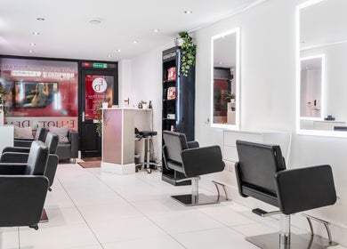 Modern salon seating area at Elliott Dean, Romford, England, GB, with stylish black chairs and illuminated mirrors.