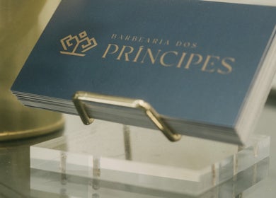 Cartões de visita da Barbearia dos Príncipes Telheiras, Lisboa, Lisboa, PT, em um suporte dourado.