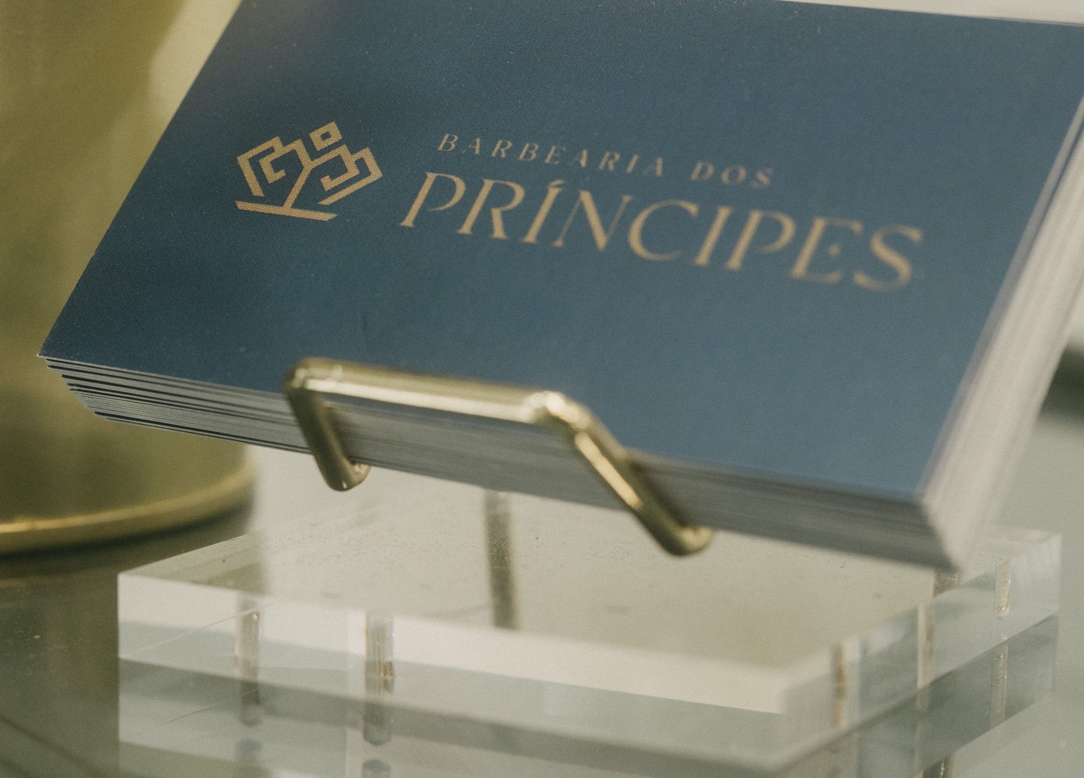 Cartões de visita da Barbearia dos Príncipes Telheiras, Lisboa, Lisboa, PT, em um suporte dourado.