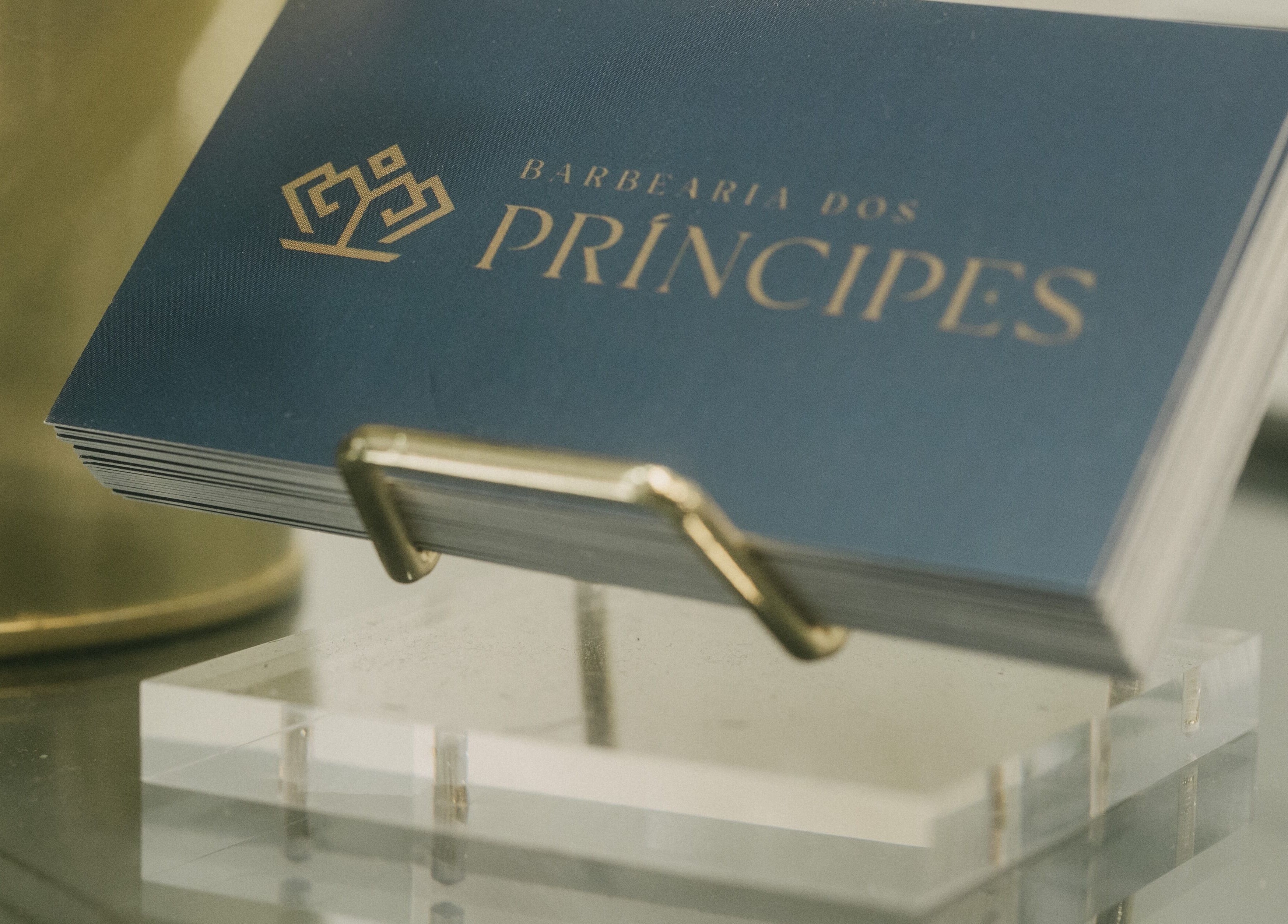 Cartões de visita da Barbearia dos Príncipes Telheiras, Lisboa, Lisboa, PT, em um suporte dourado.