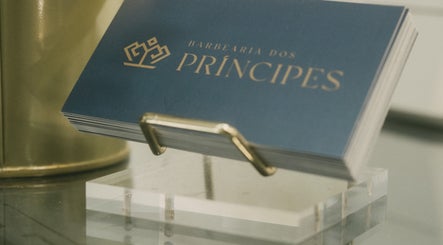 Cartões de visita da Barbearia dos Príncipes Telheiras, Lisboa, Lisboa, PT, em um suporte dourado.