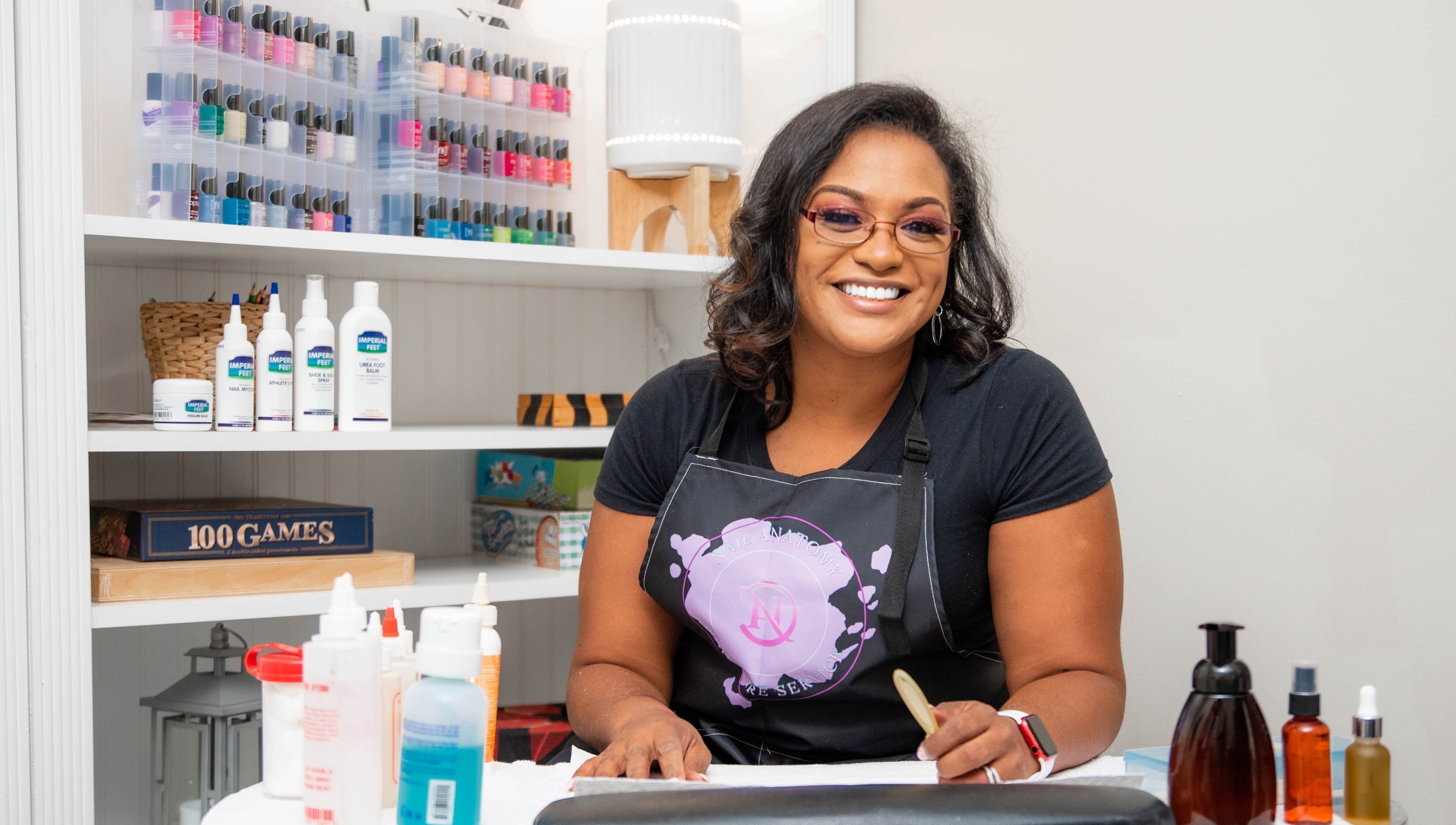 Smiling woman at Nail Anatomy - Mobile in Stockbridge, Georgia, US, with nail polish in background.