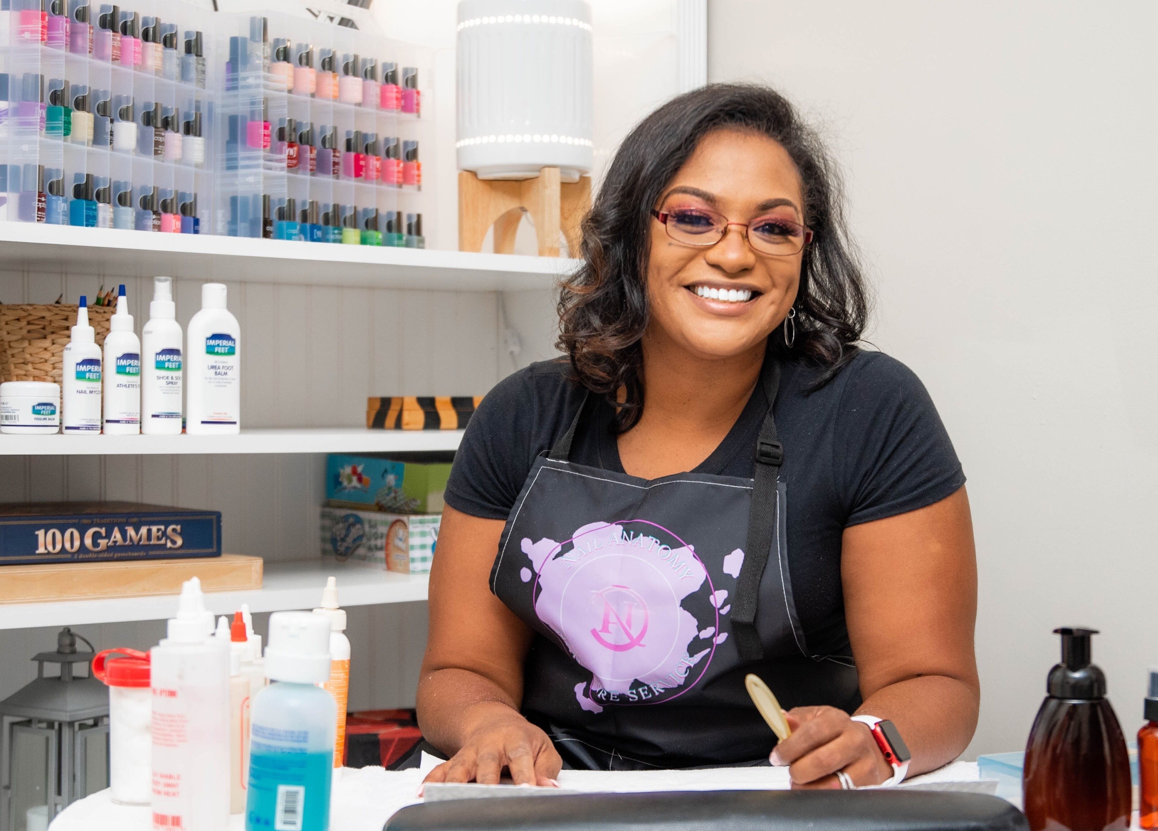 Smiling woman at Nail Anatomy - Mobile in Stockbridge, Georgia, US, with nail polish in background.