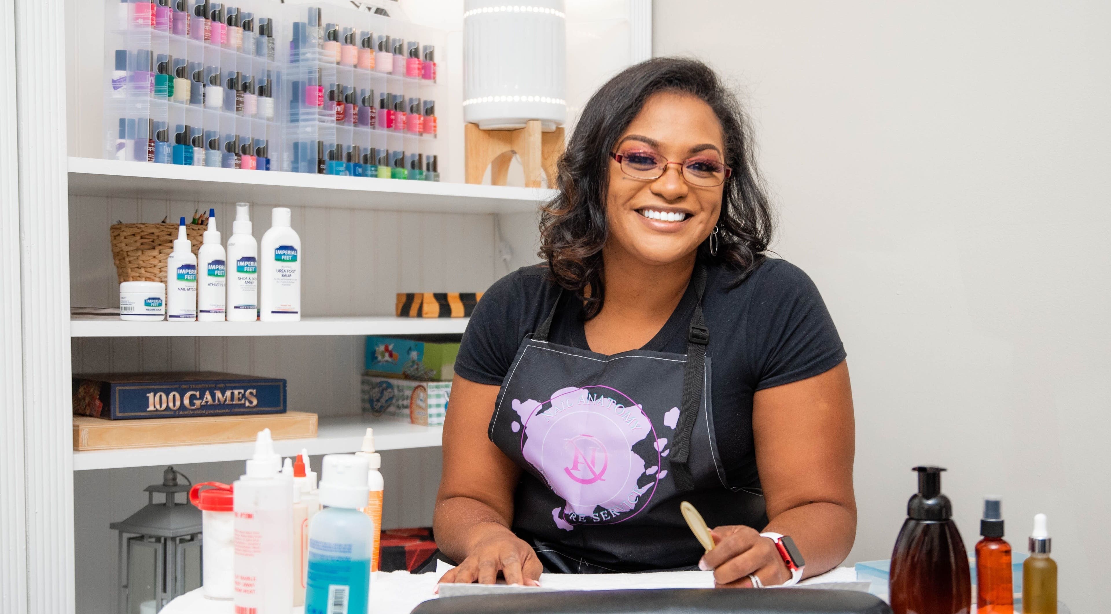 Smiling woman at Nail Anatomy - Mobile in Stockbridge, Georgia, US, with nail polish in background.