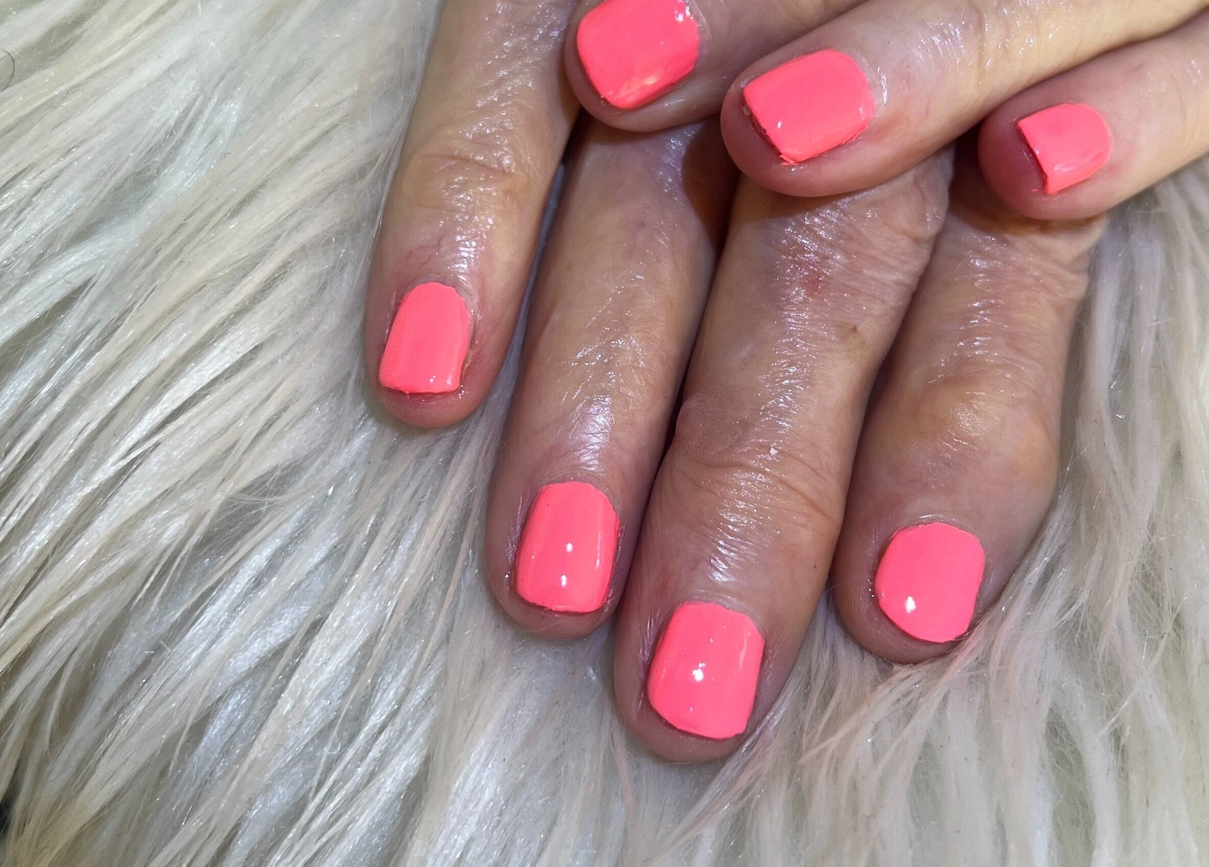 Bright pink manicured nails at Nail Anatomy - Mobile in Stockbridge, Georgia, US, displayed on white fur.
