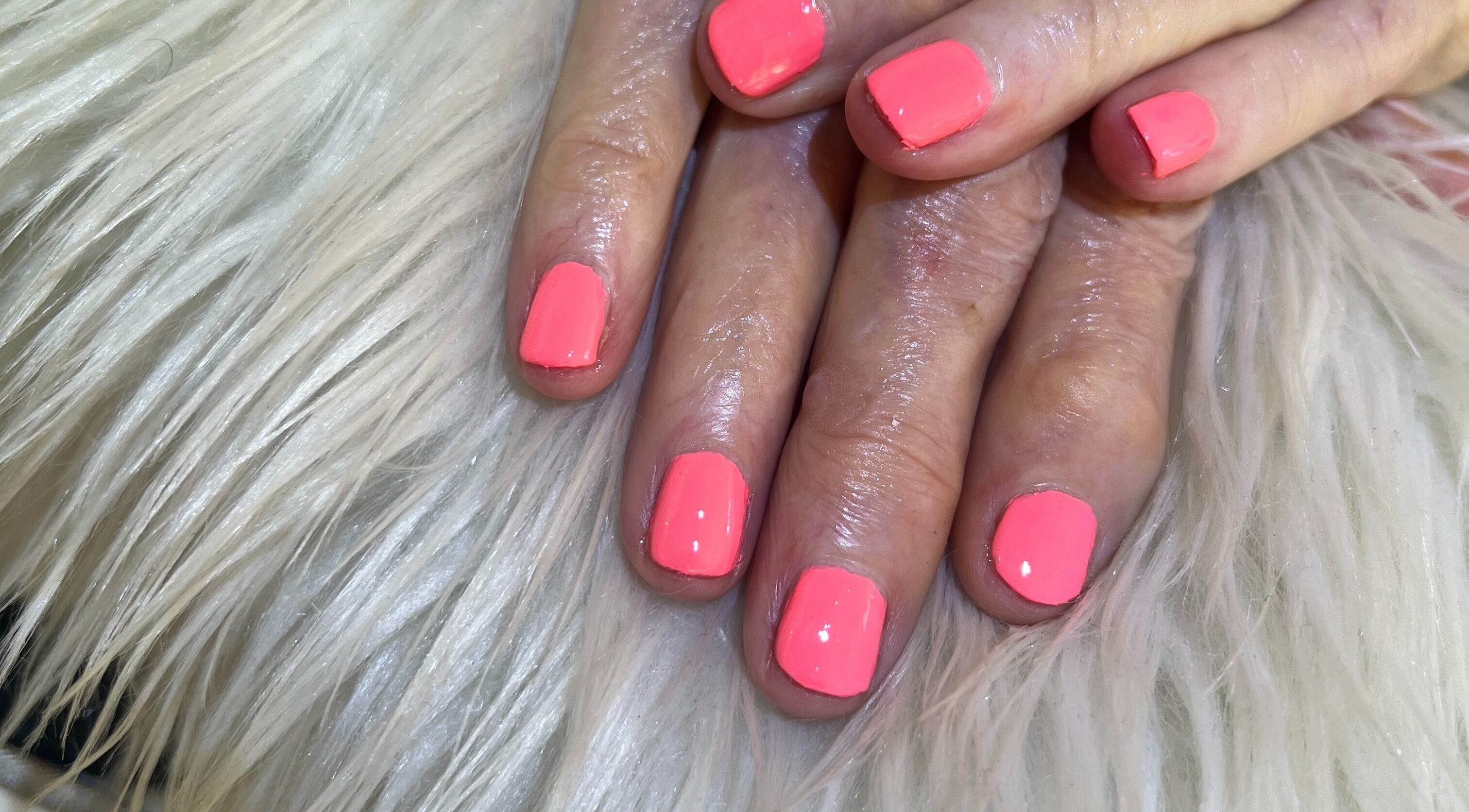 Bright pink manicured nails at Nail Anatomy - Mobile in Stockbridge, Georgia, US, displayed on white fur.