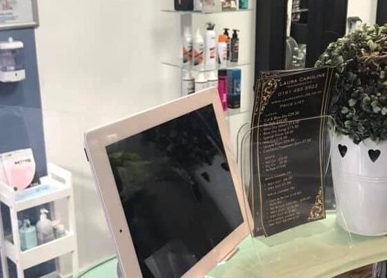 Reception desk at Laura Caroline Hairdressing in Cheadle Hulme, England, GB showcasing salon menu and plants.