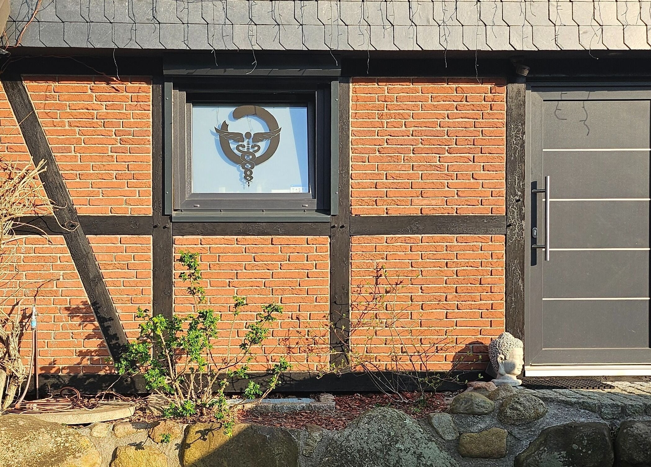 Eingang von Body Mind Academy in Kiel, Schleswig-Holstein, DE mit rustikaler Ziegelwand und Buddha-Statue.