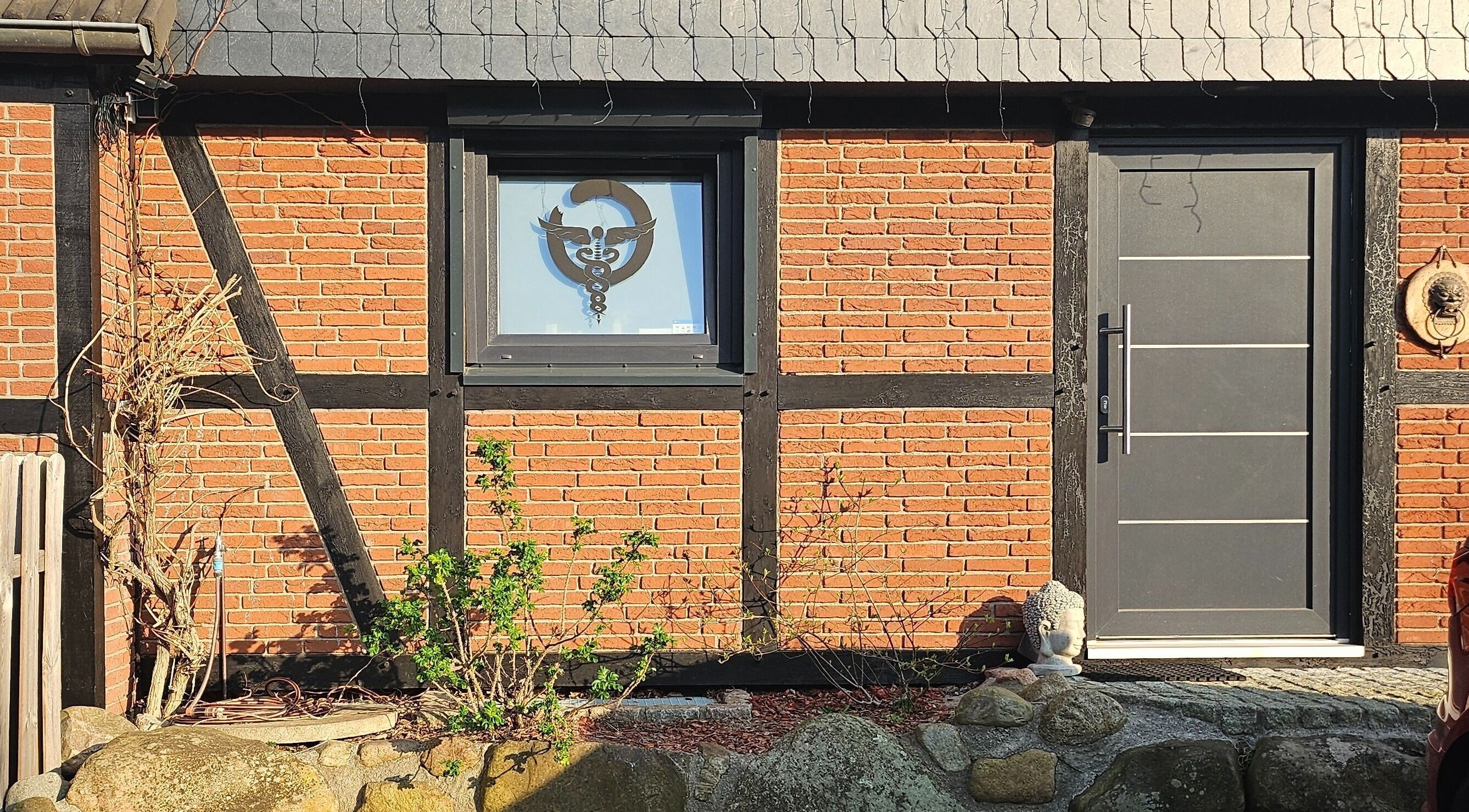 Eingang von Body Mind Academy in Kiel, Schleswig-Holstein, DE mit rustikaler Ziegelwand und Buddha-Statue.