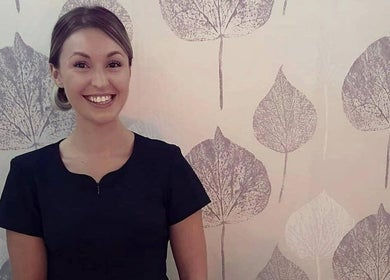 Smiling therapist at Rio Bluebell Therapies, Salisbury, England, GB, against leaf-patterned wall.