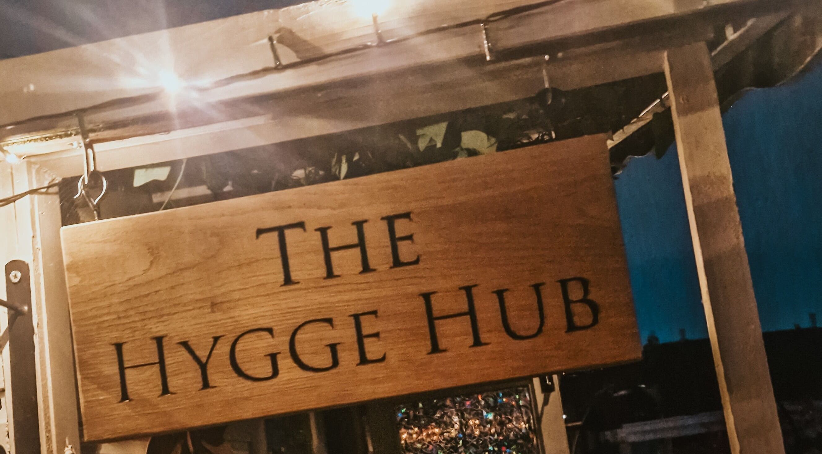 Wooden signboard of The Hygge Hub, a cozy venue in Littleborough, England, GB, warmly lit at night.