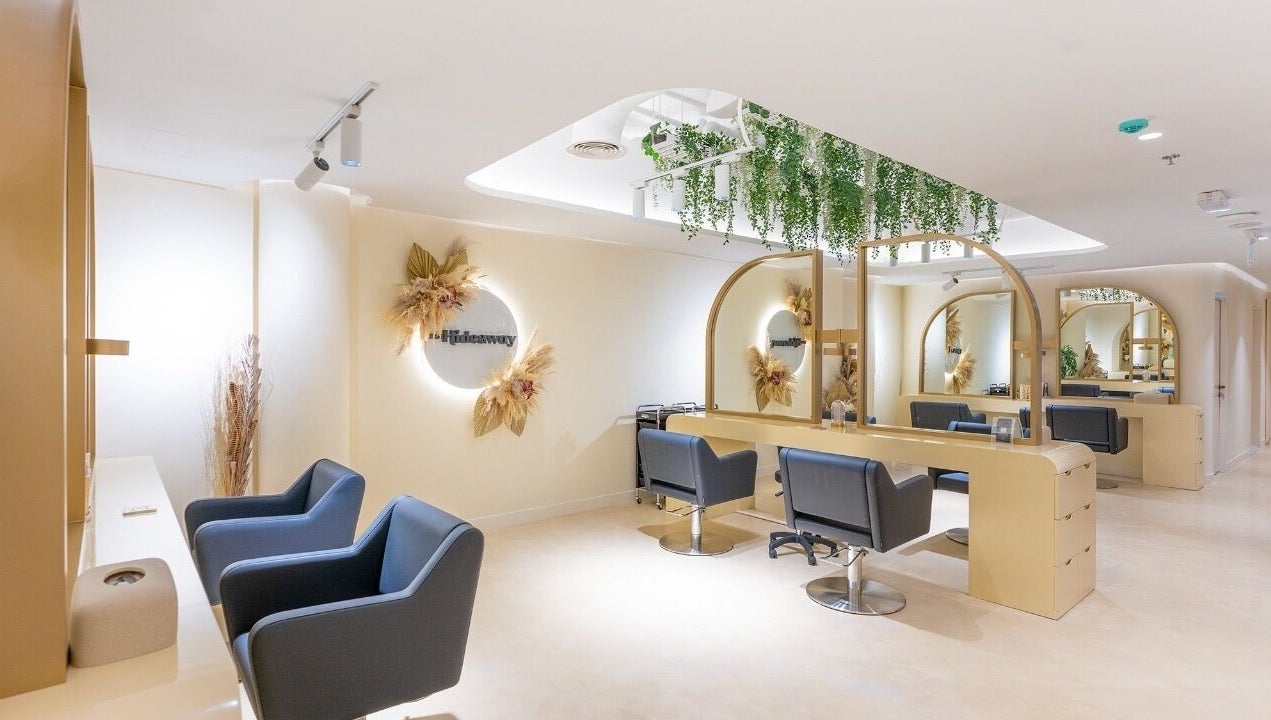 Chic salon interior of The Hideaway, Dubai, AE, with sleek chairs and mirrors under lush greenery.