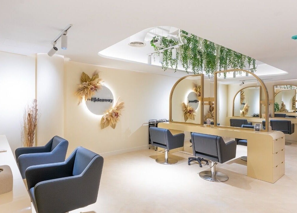 Chic salon interior of The Hideaway, Dubai, AE, with sleek chairs and mirrors under lush greenery.