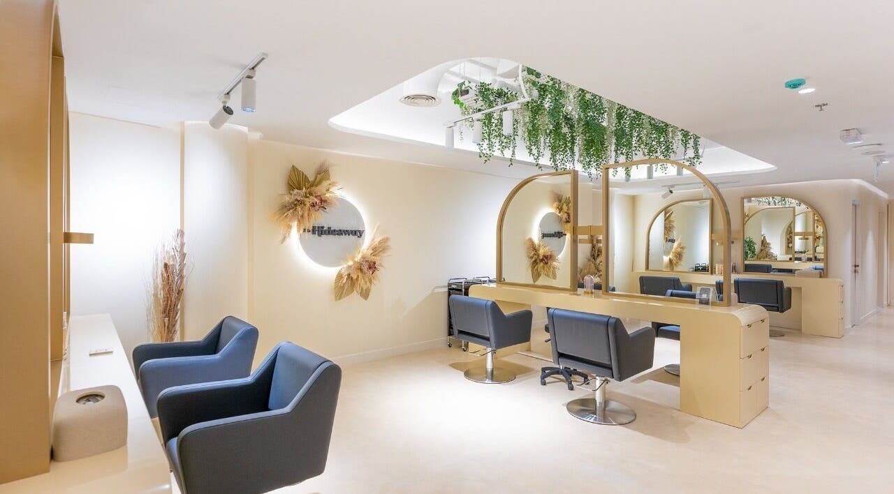 Chic salon interior of The Hideaway, Dubai, AE, with sleek chairs and mirrors under lush greenery.