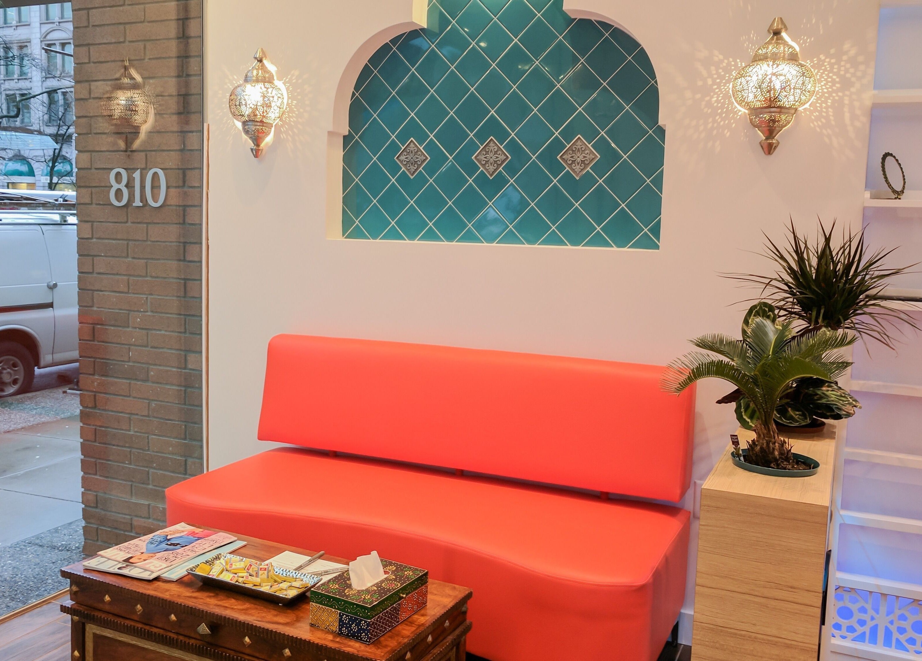 Cozy waiting area at Blink Brow Bar Bute St in Vancouver, with red seating, teal tiles, and elegant decor elements.