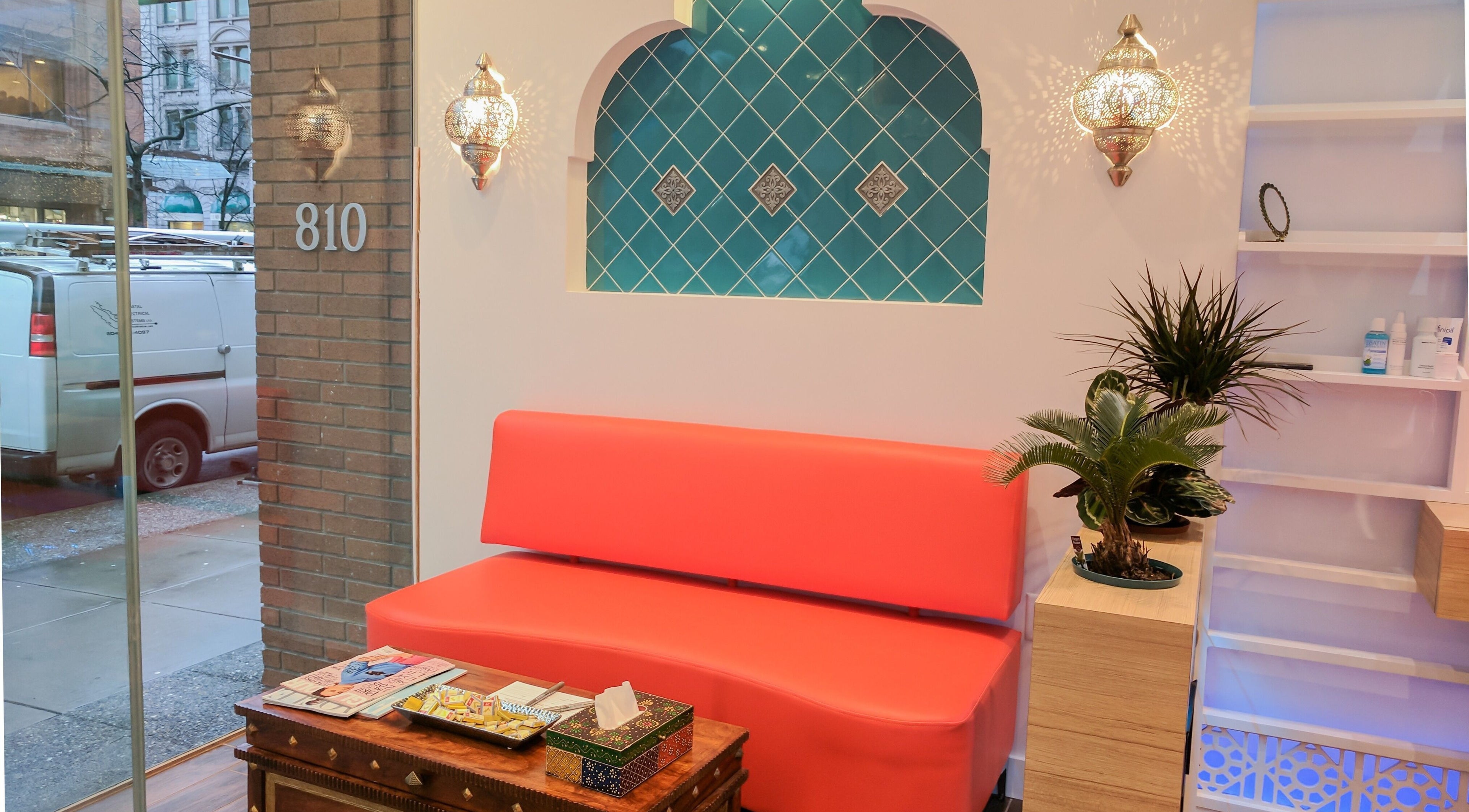 Cozy waiting area at Blink Brow Bar Bute St in Vancouver, with red seating, teal tiles, and elegant decor elements.