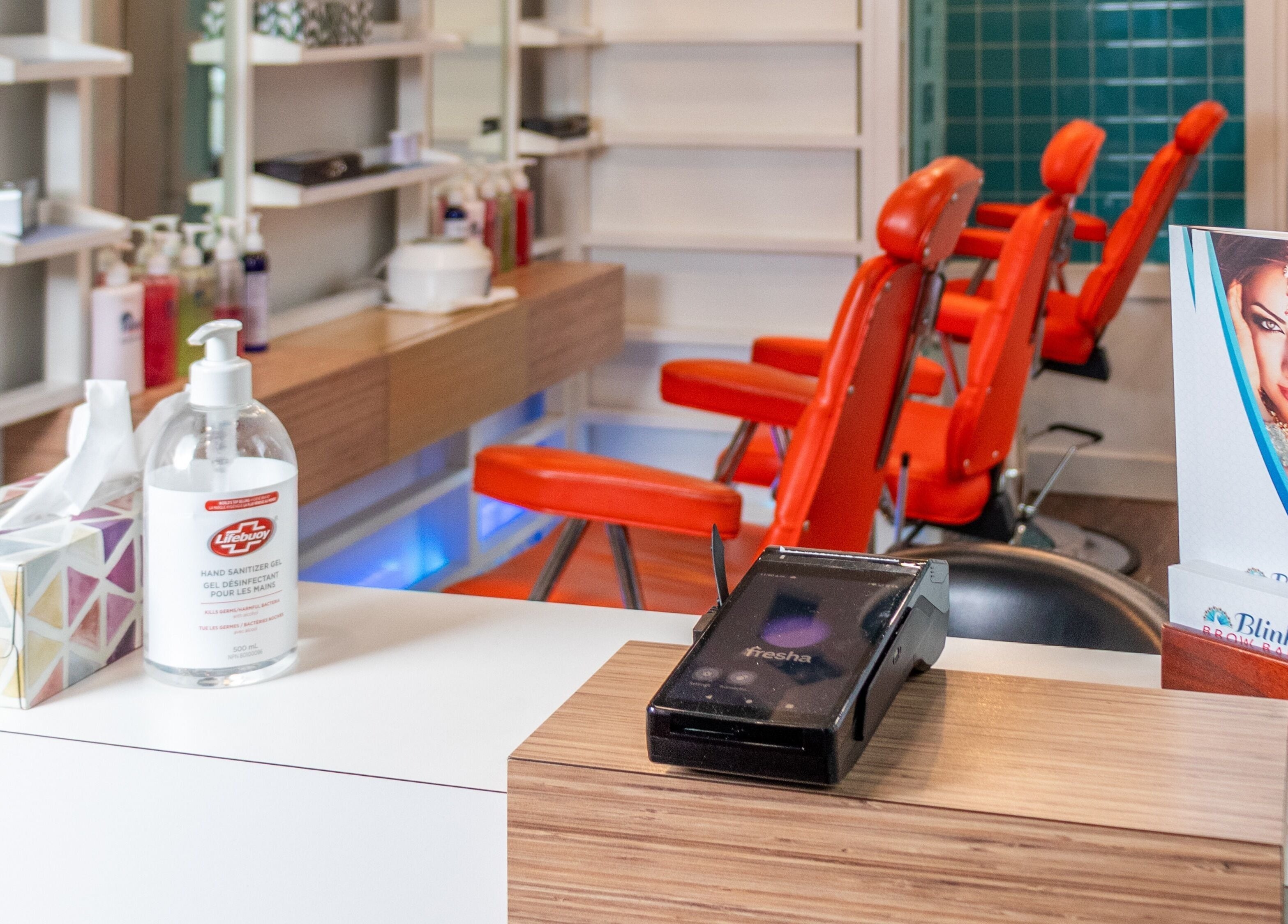 Interior of Blink Brow Bar Bute St in Vancouver, British Columbia, CA with vibrant red chairs and beauty products.