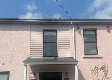Exterior view of COCO ROSE BEAUTY, a pastel pink building in St Austell, England, GB, under a bright sky.