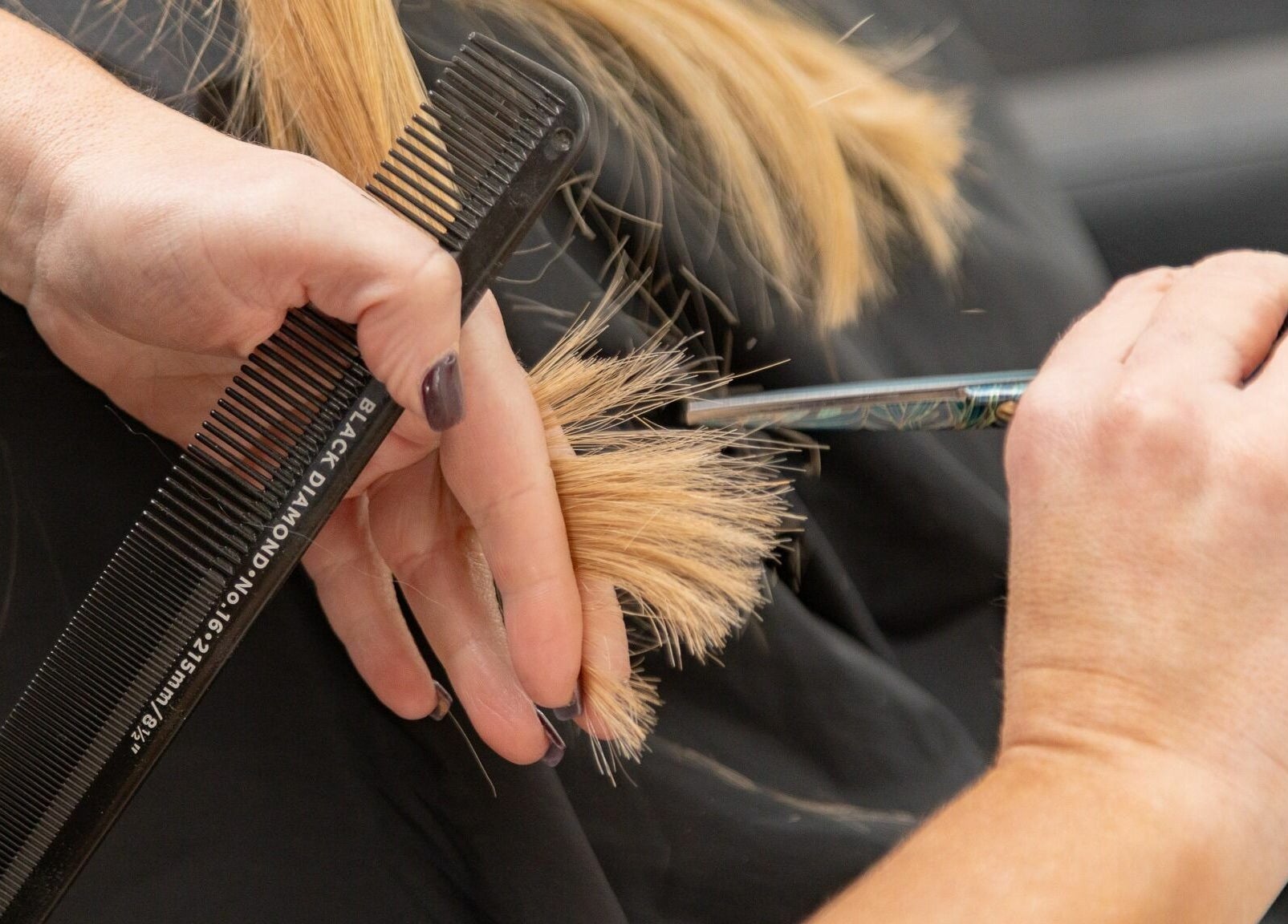 Hairstylist performing precision haircut at Tusk Salon, Moreton, England, GB with scissors and comb.