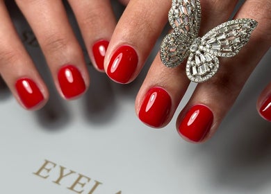 Stylish red manicured nails at Eyelash Secret Ladies Salon Iris Bay, Dubai, Dubai, AE, with a butterfly ring.