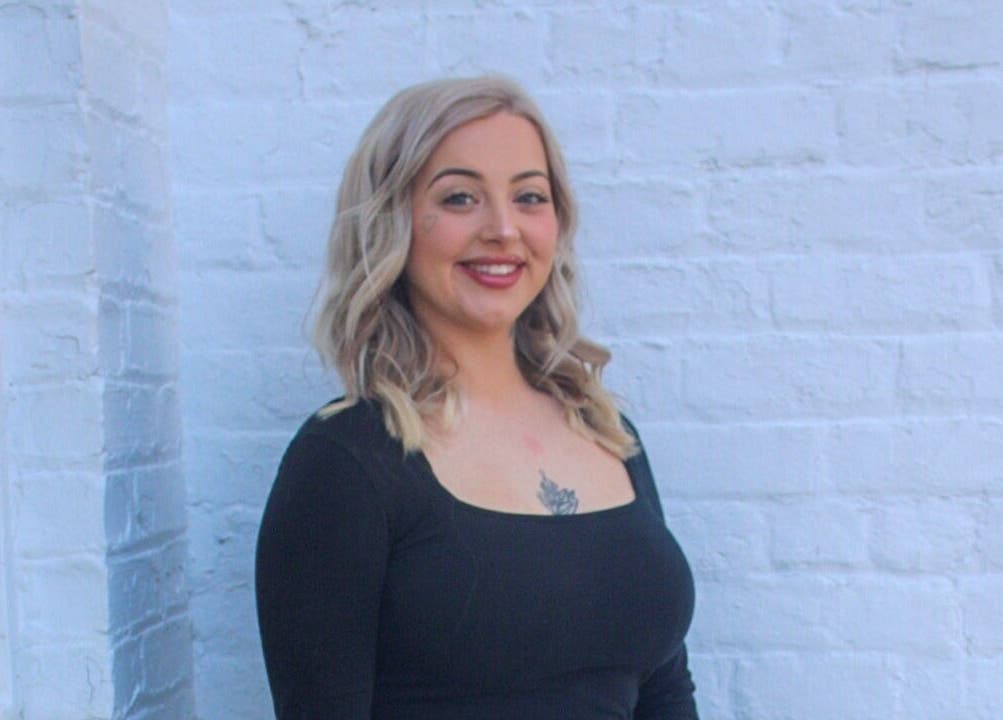 Experienced stylist at So Kno Bliss Salon in Knoxville, Tennessee, US stands against a chic white brick wall.